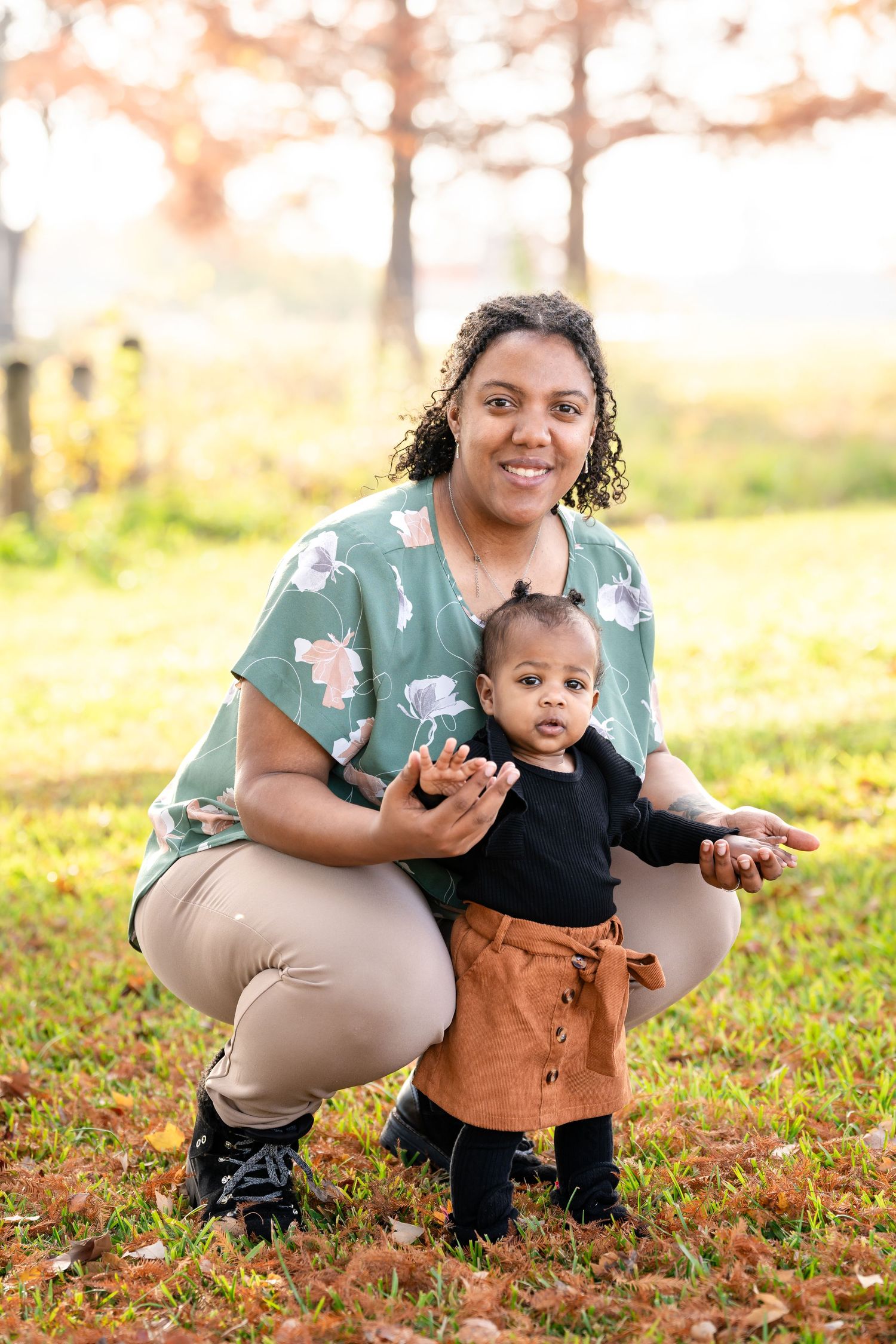An autumn outdoor portrait with someone wearing a mint floral top crouching on fallen leaves.