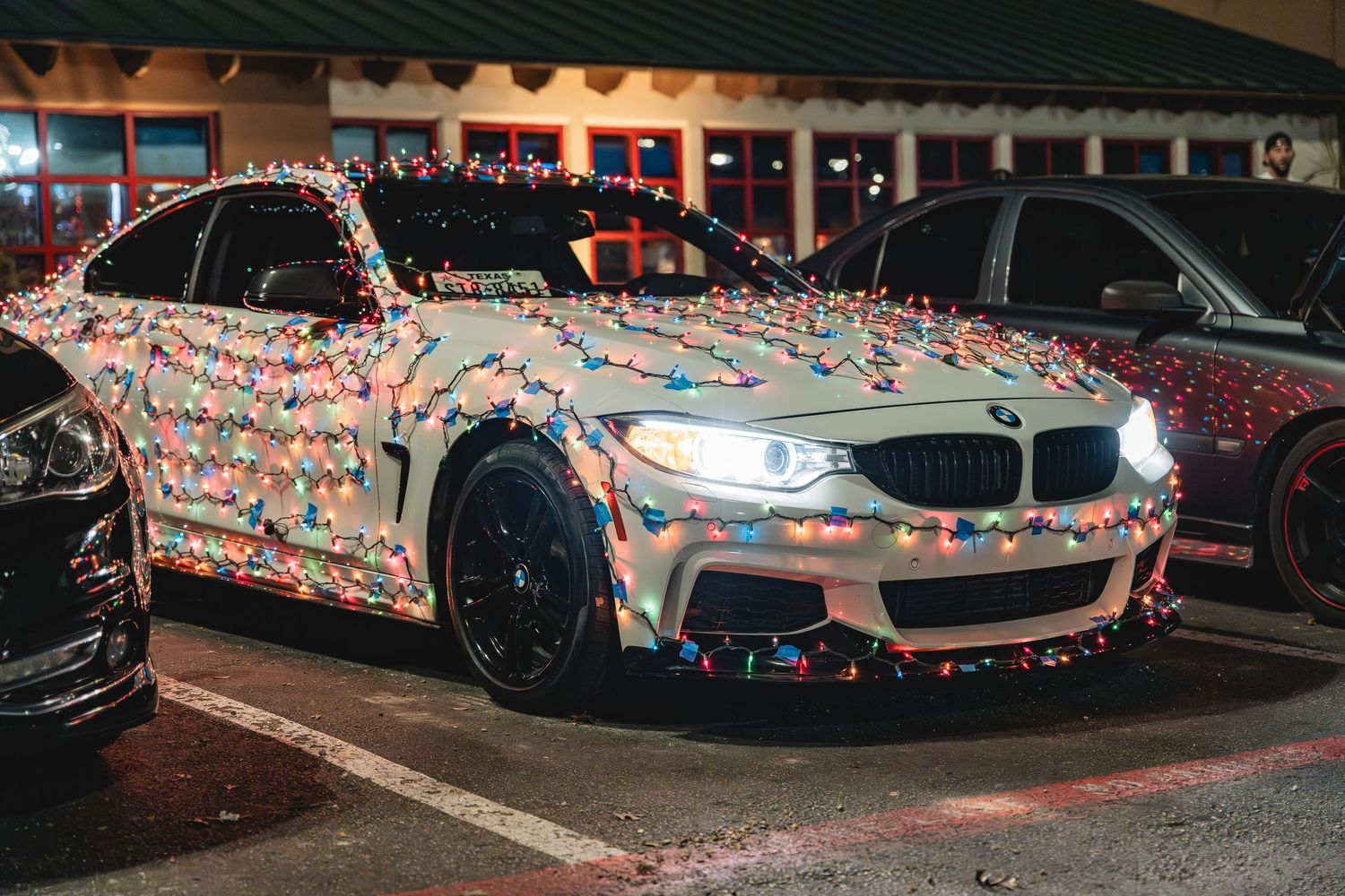BMW M car decorated with colorful Christmas lights parked at night.