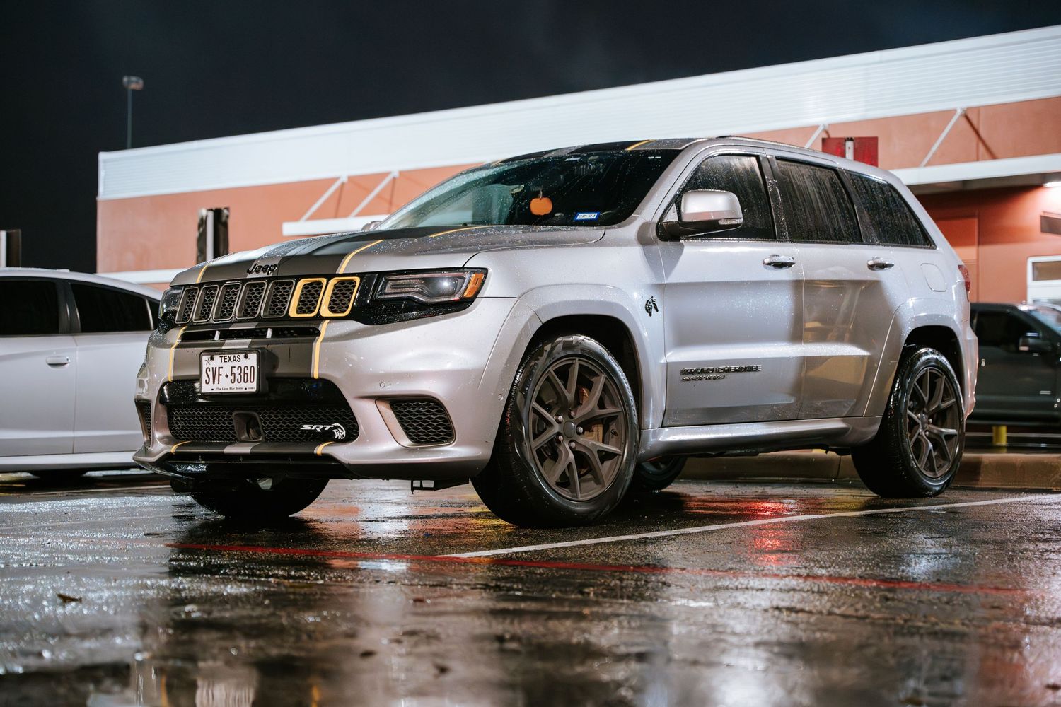 Silver Jeep Grand Cherokee SRT parked in a wet parking lot at night.