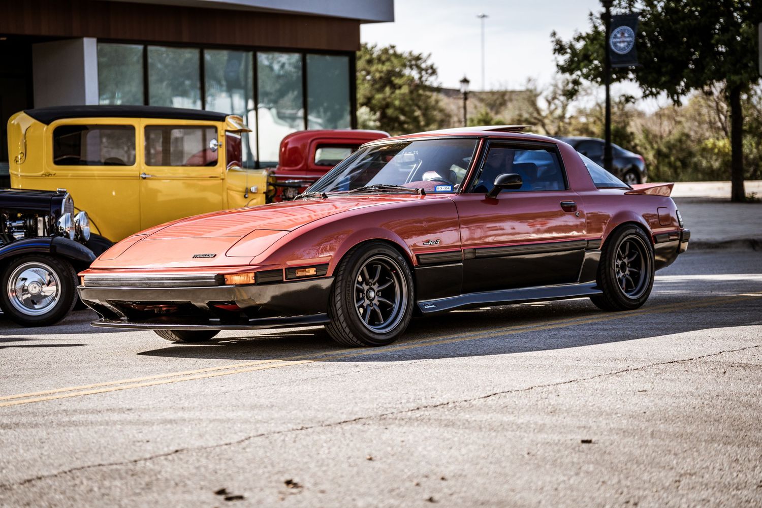 Vintage copper-colored Mazda RX-7 sports car parked at a car show.