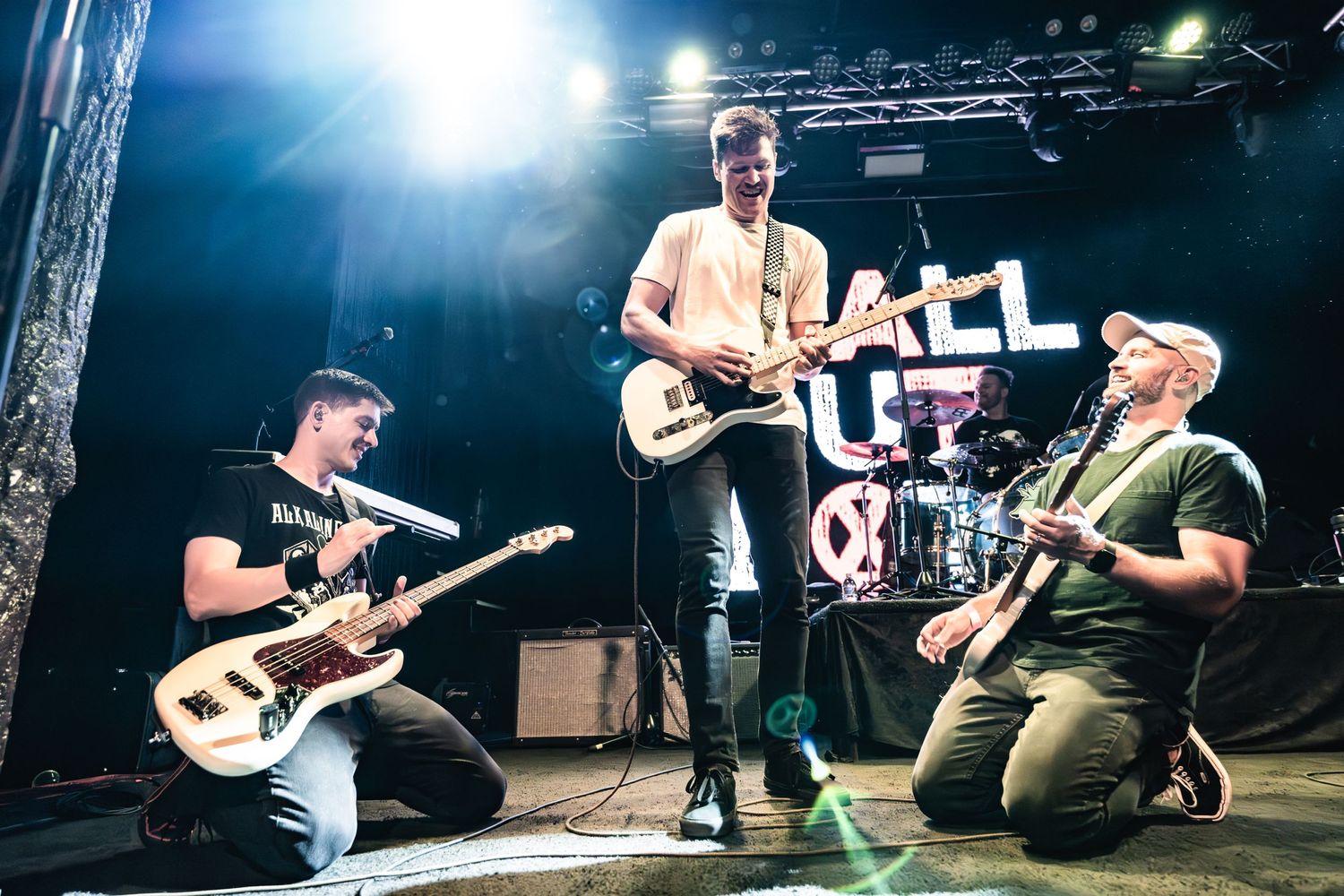 Rock band performs energetically on stage with multiple guitarists under bright stage lighting.