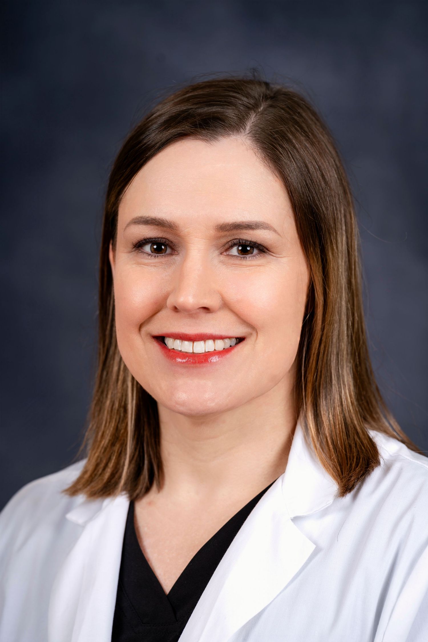 Medical professional portrait in white lab coat and black top against dark studio background.
