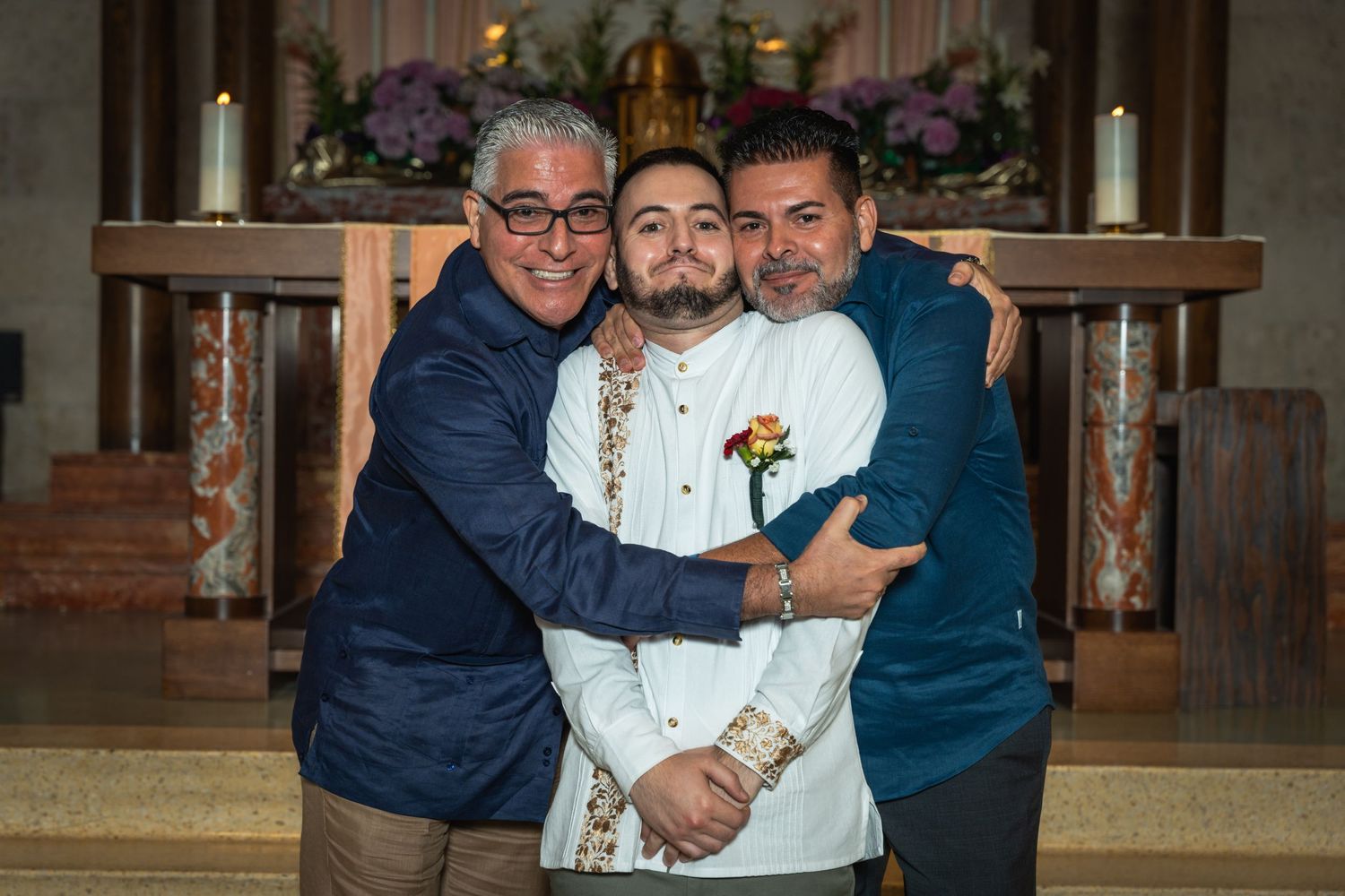 Three people share an emotional embrace at church altar during celebration.