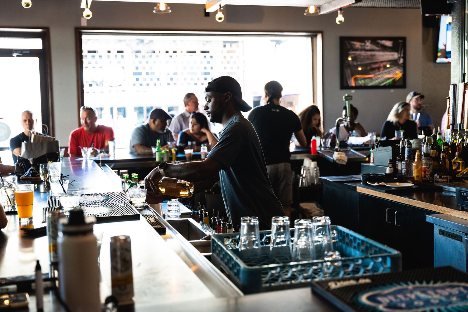 Bartender prepares drinks behind counter in a well-lit modern bar setting.