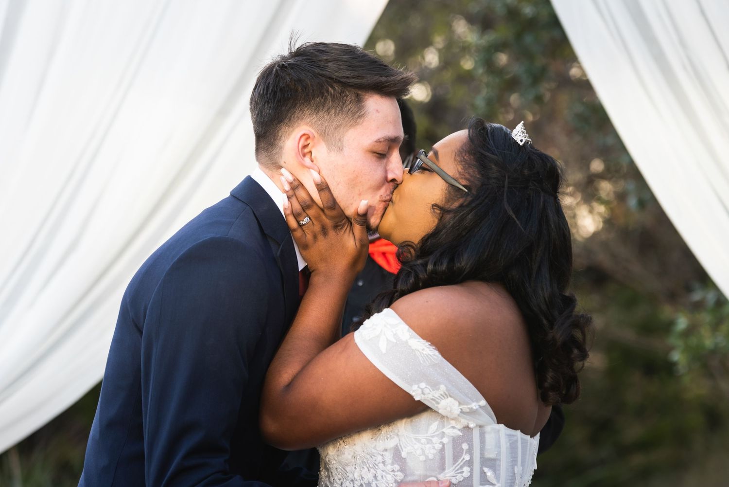 An intimate kiss between newlyweds captured under elegant white drapes during their wedding ceremony.
