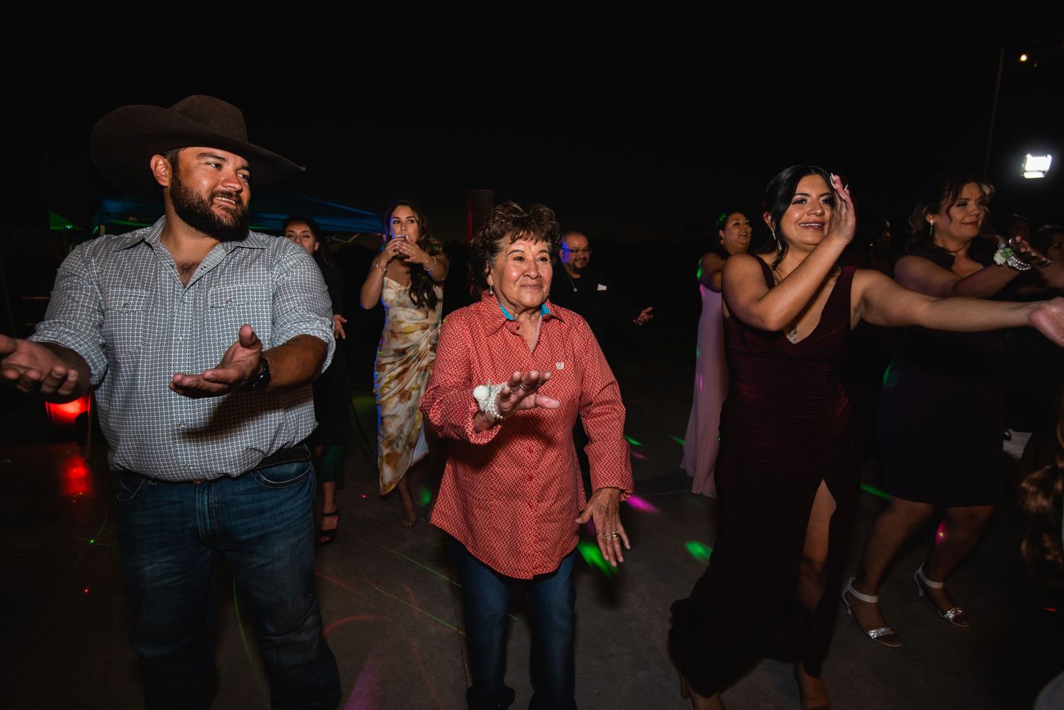 Wedding guests dancing enthusiastically during nighttime outdoor reception celebration.