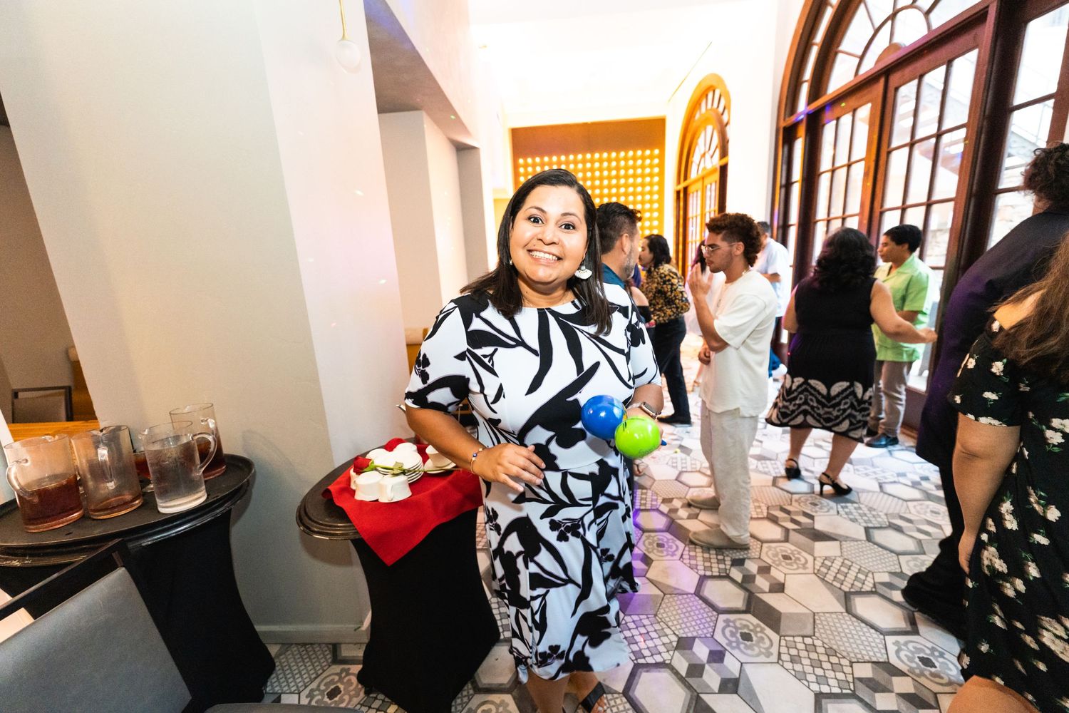 A guest in a black and white patterned dress enjoys a gathering in an elegant room with arched windows.