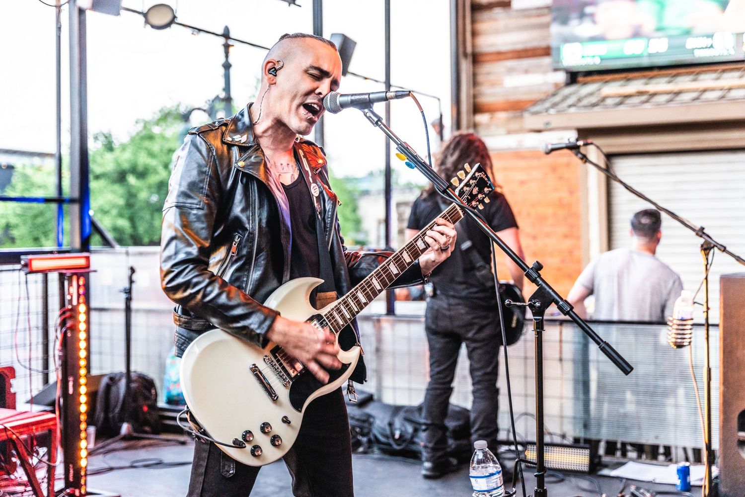 Rock musician plays guitar during outdoor performance on sunlit stage.