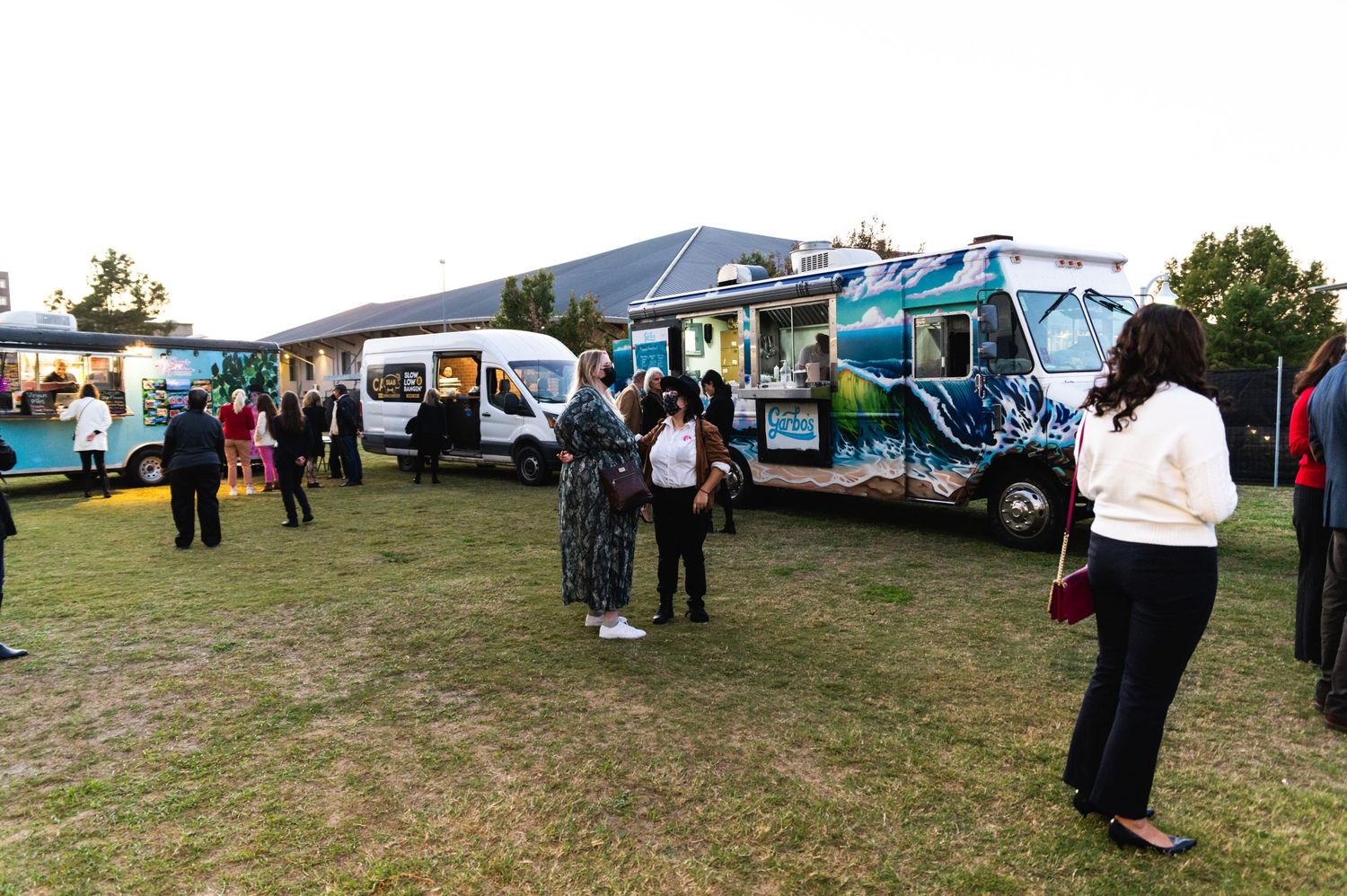 Food trucks and visitors gather at an outdoor festival event on grassy field.
