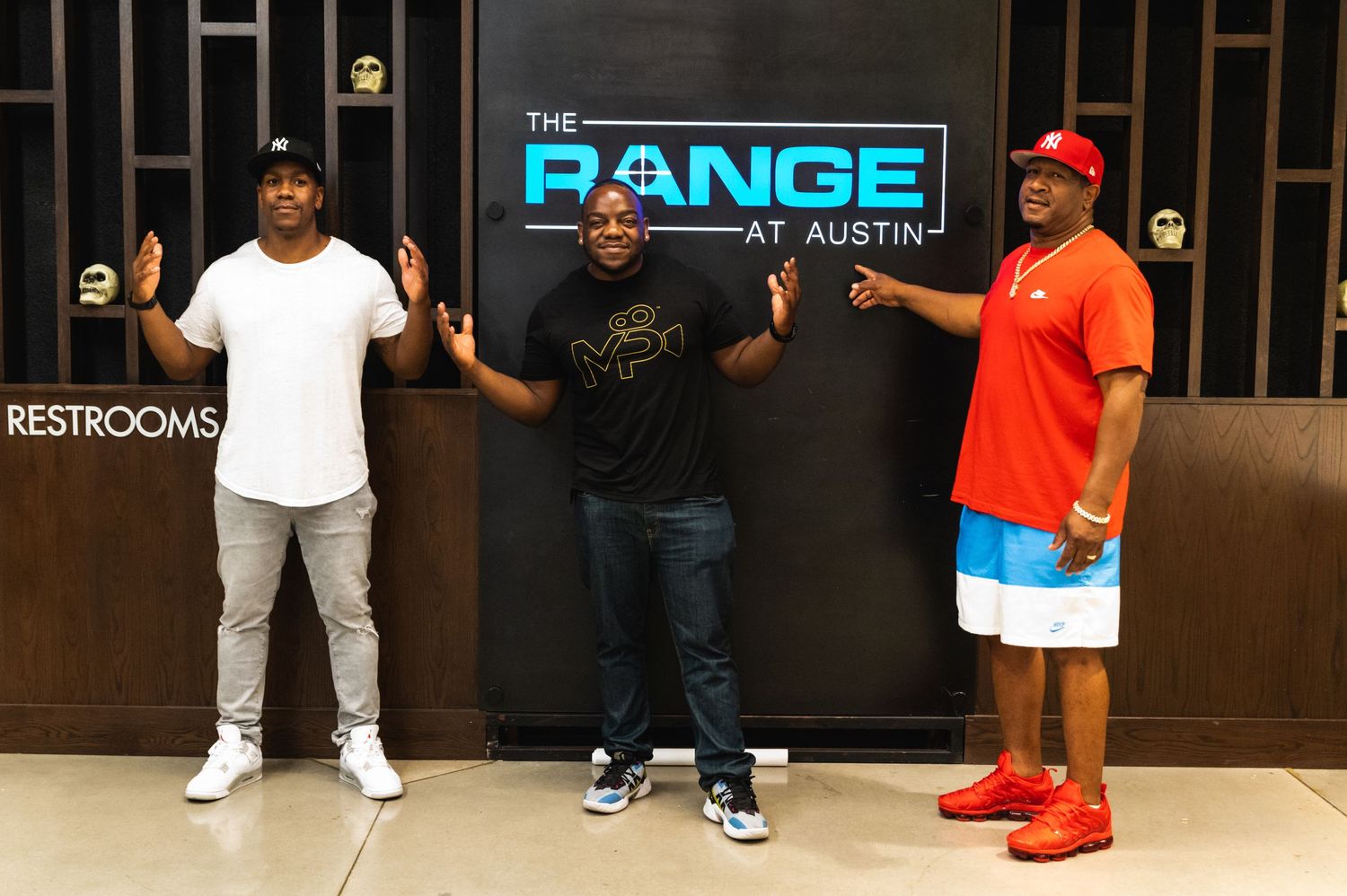Three people posing in front of illuminated Range sign at facility entrance.