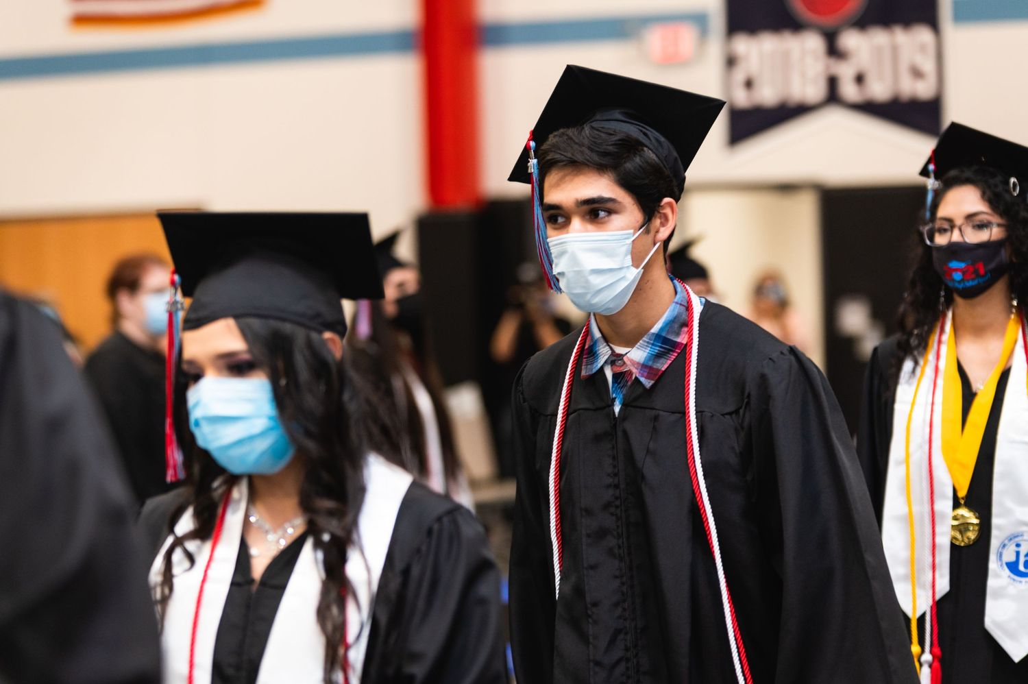 Masked graduates in traditional black caps and gowns during graduation ceremony.