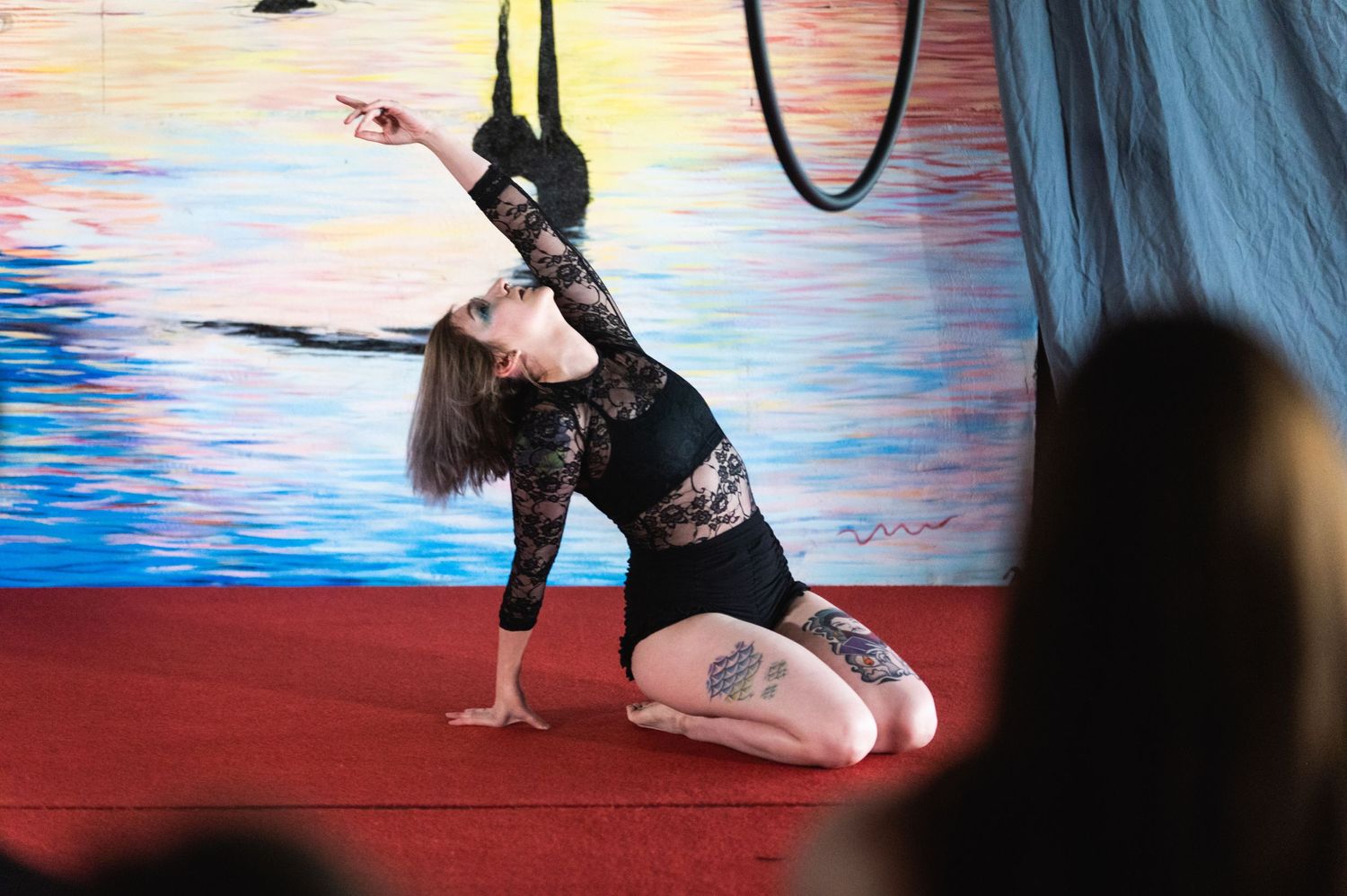 Dancer in black lace performs floor routine with aerial straps against colorful background.