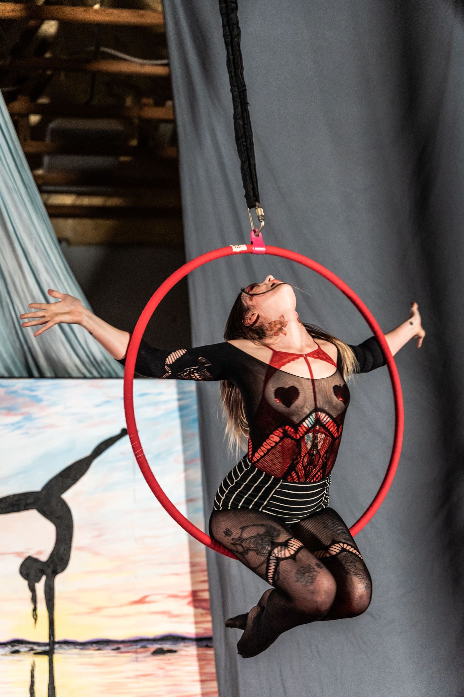 An acrobatic performer executing a dramatic pose while suspended from a red aerial hoop.