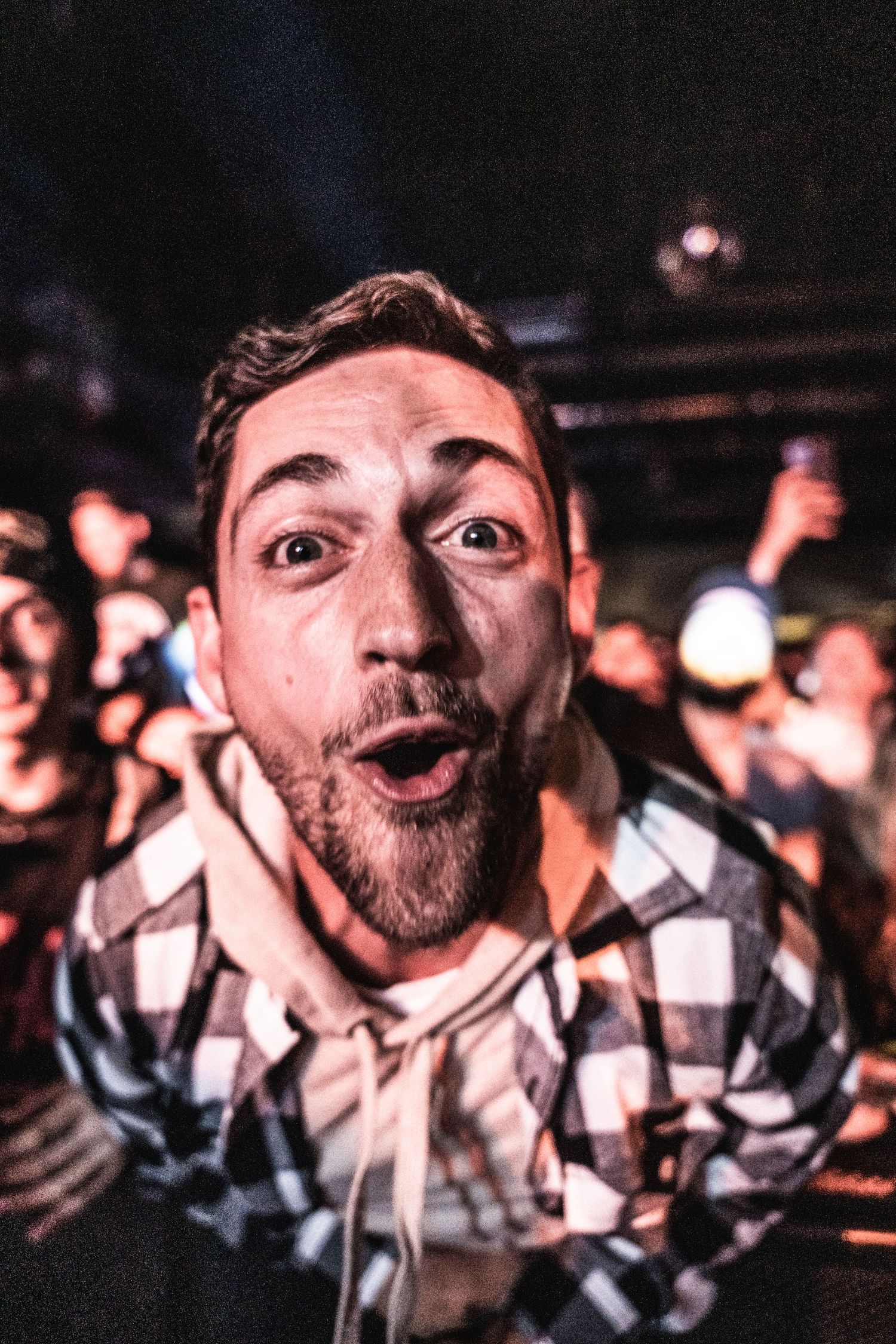 Concert attendee in checkered shirt expressing excitement during live music event.