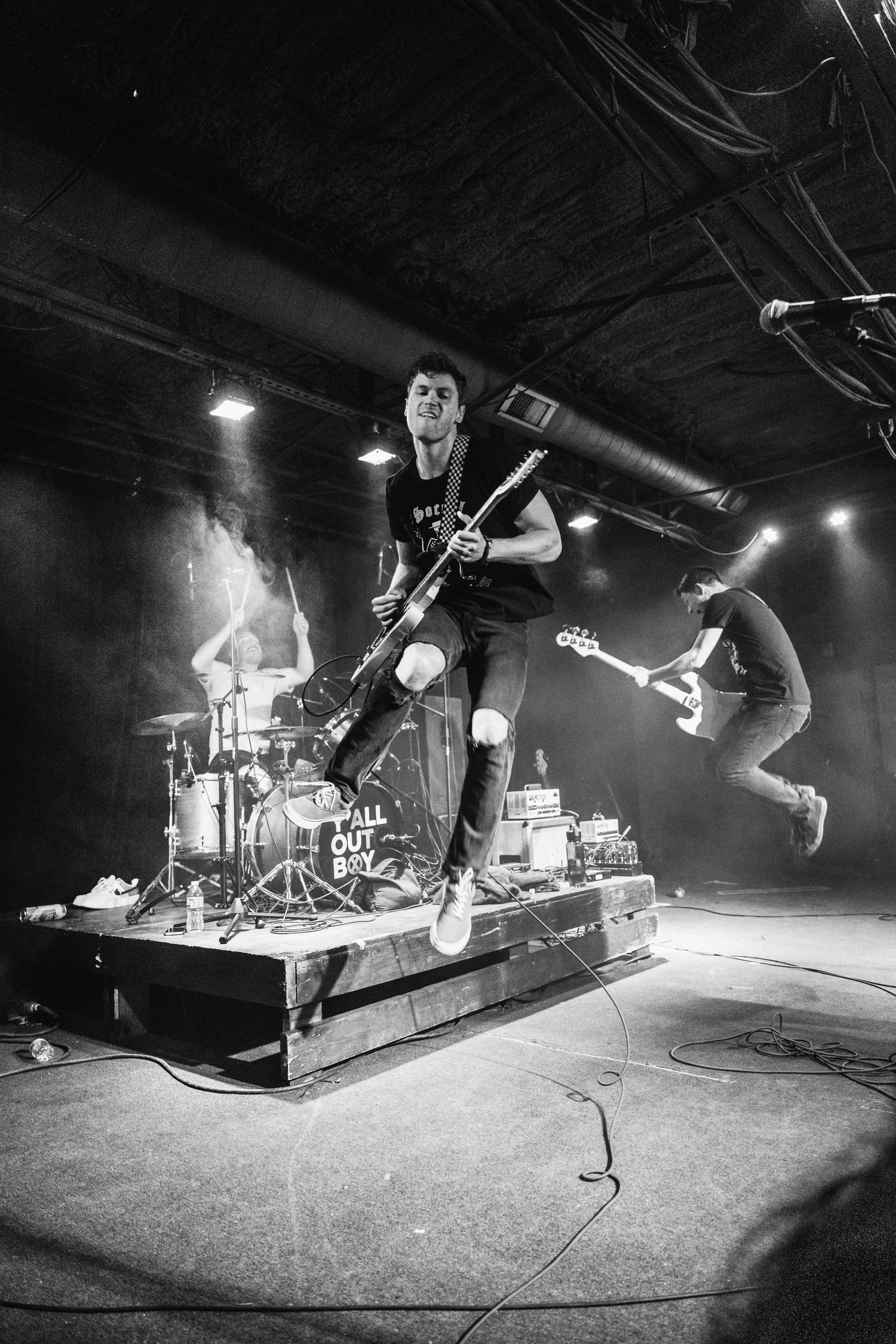 High-energy black and white concert photo of musicians jumping during performance on stage.