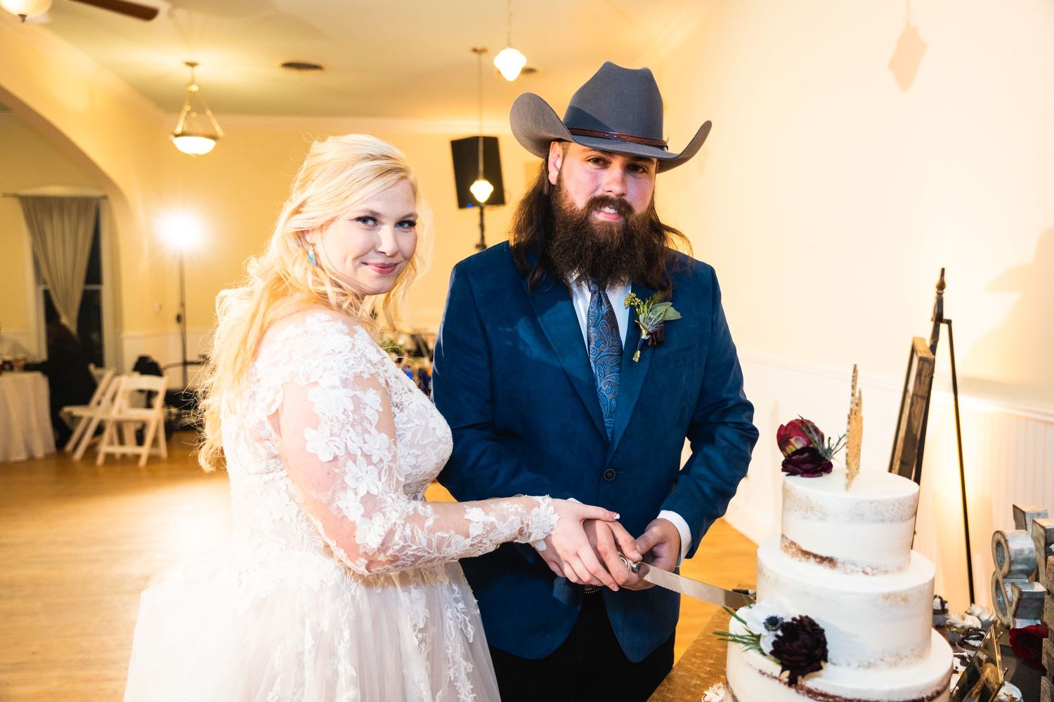 A couple cuts their white wedding cake together at their rustic-themed reception.
