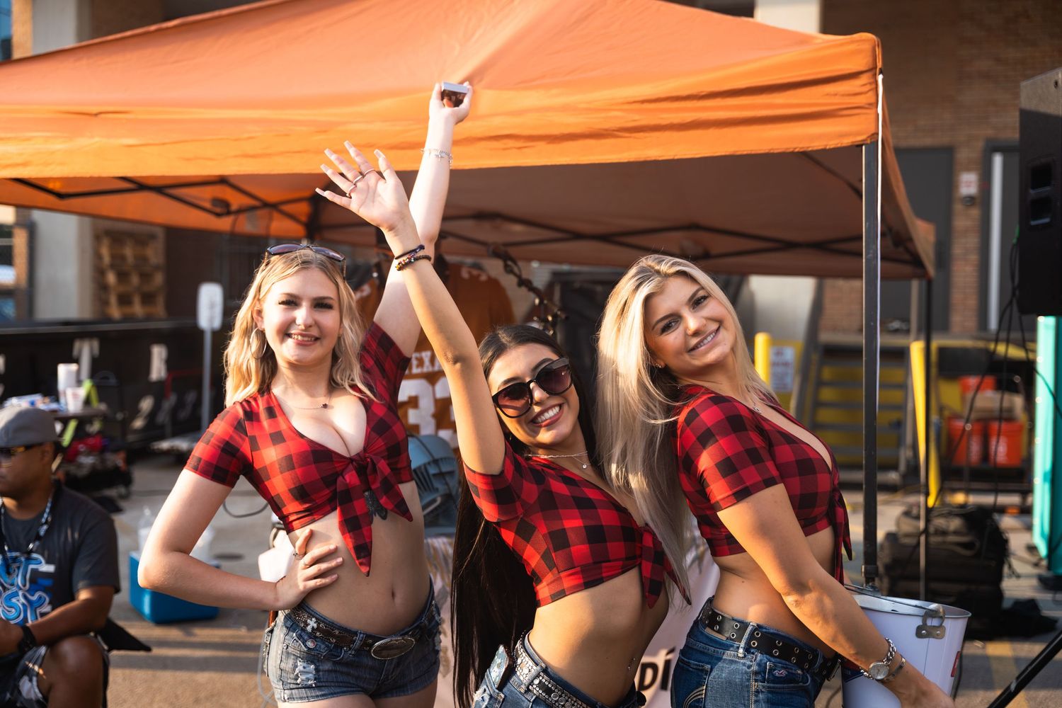Three people in matching red plaid tops posing together at outdoor celebration.