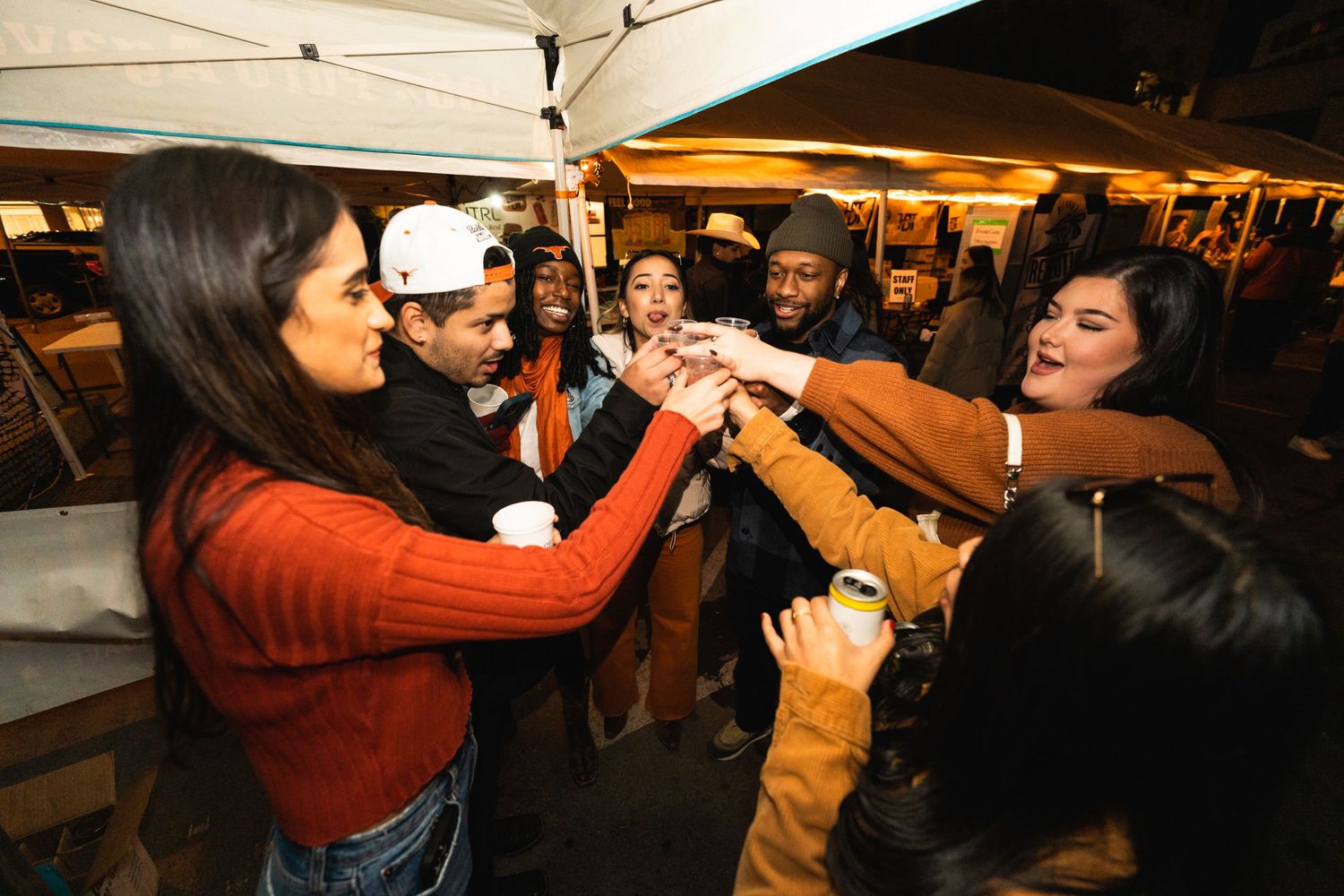 A group toasting and clinking drinks together at an outdoor gathering.