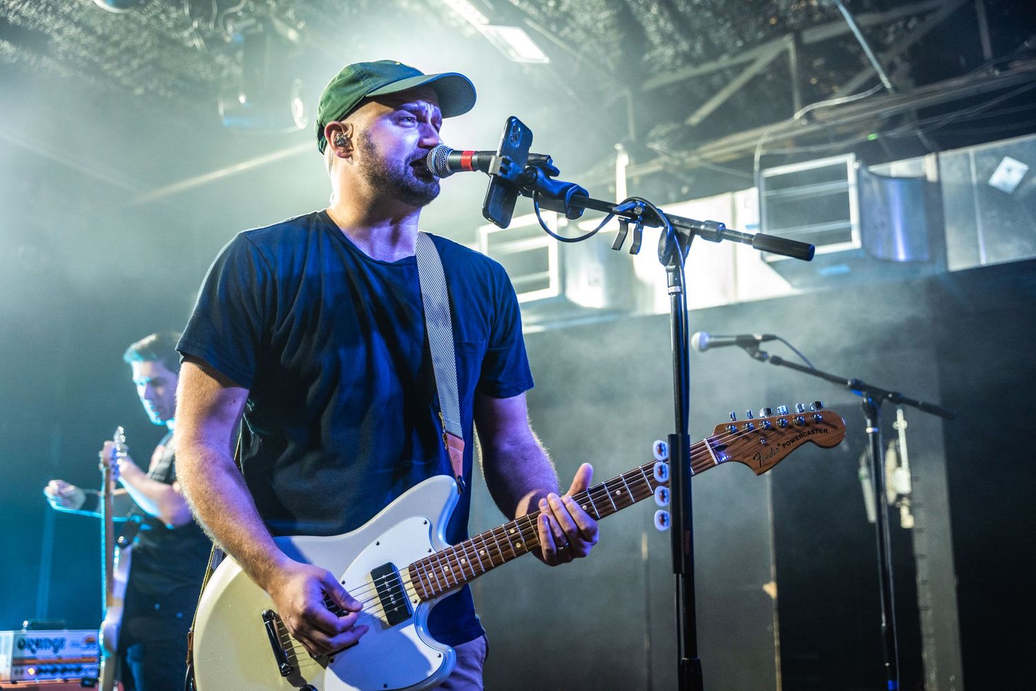 Guitar player performs with backlit blue lighting effects on stage during live concert performance.