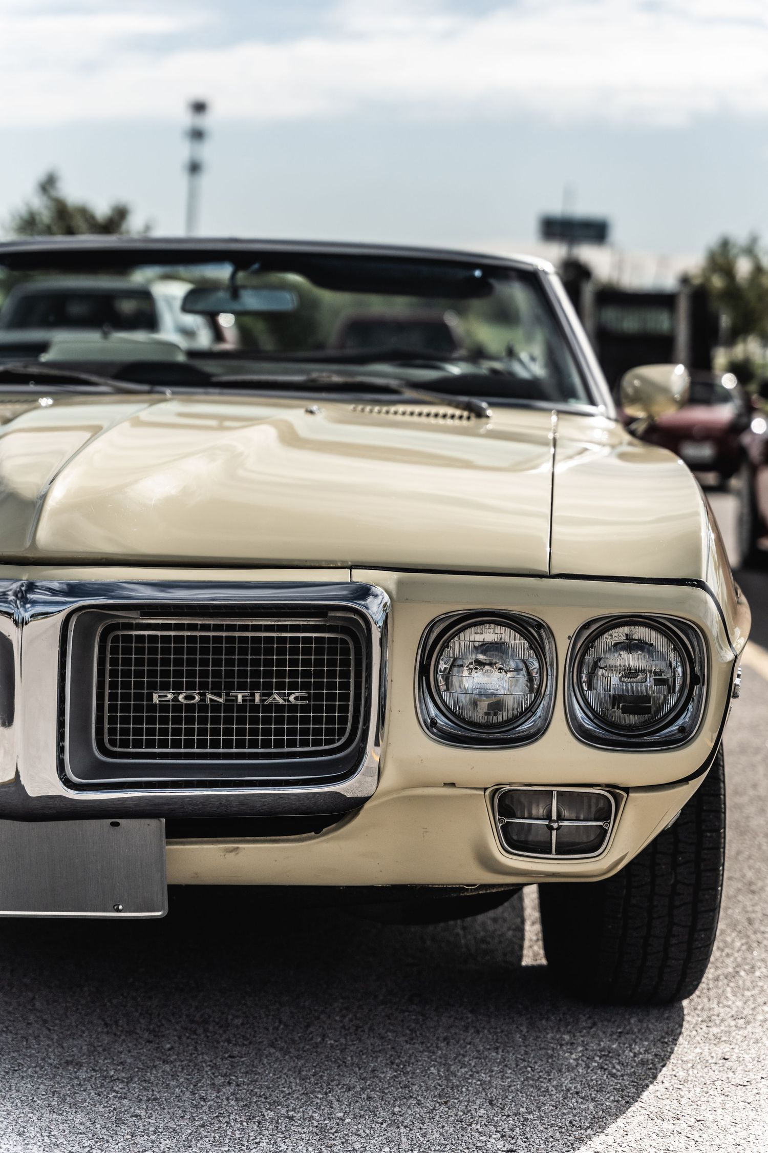 Front end detail of cream-colored vintage Pontiac Firebird showing distinctive dual headlights.