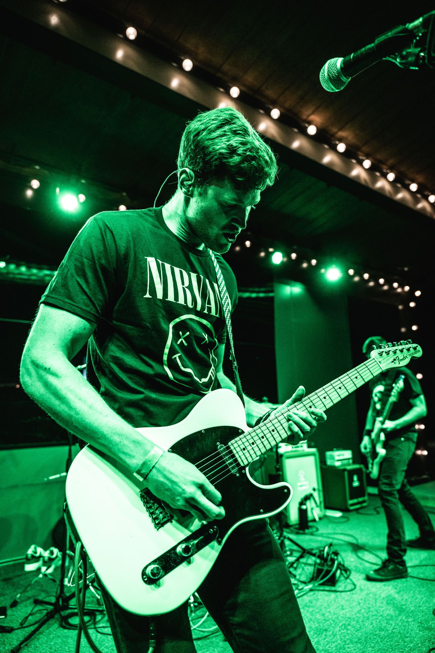 Guitar player wearing Nirvana t-shirt performs under green stage lighting.