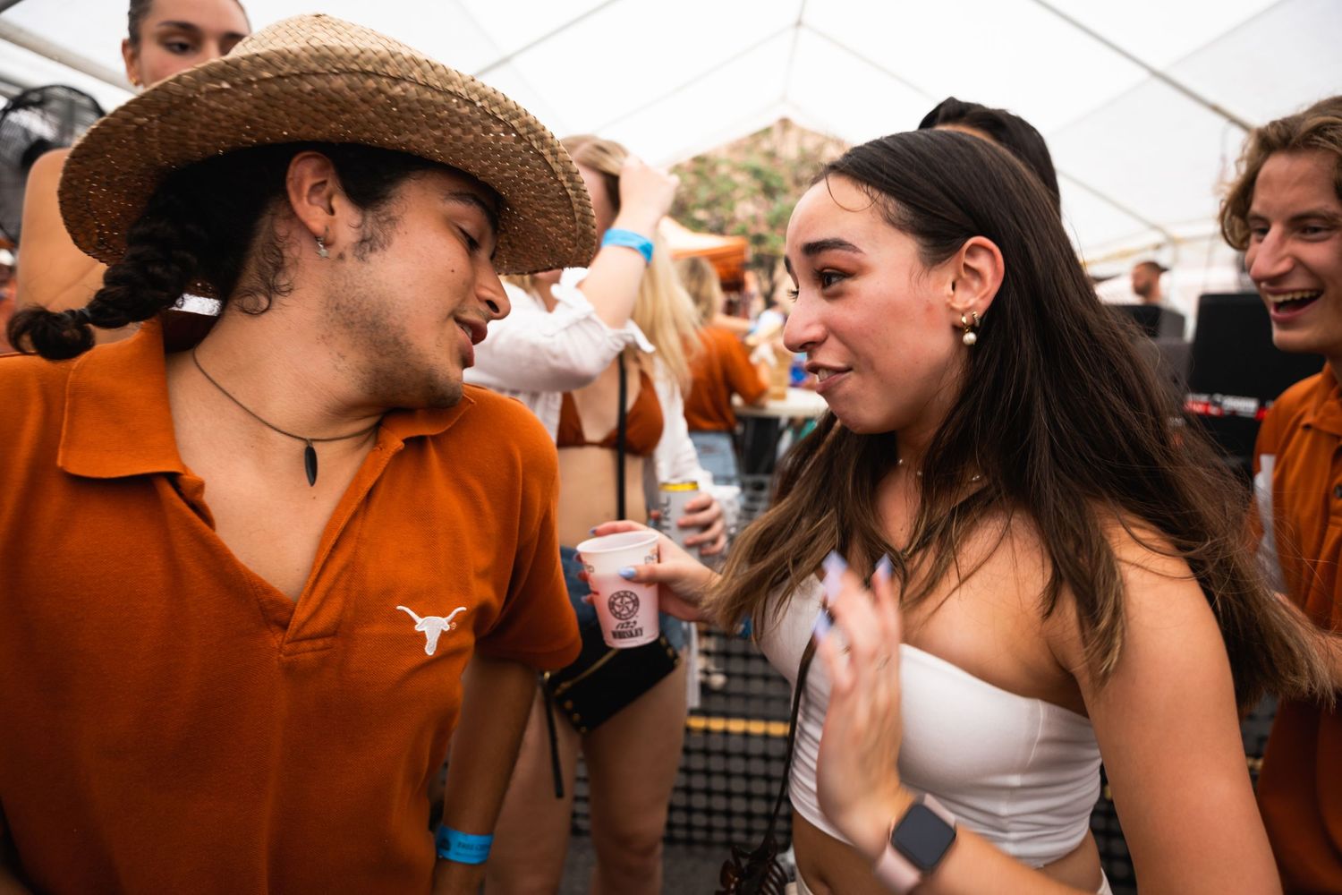People enjoying conversation and drinks at outdoor gathering under white tent.