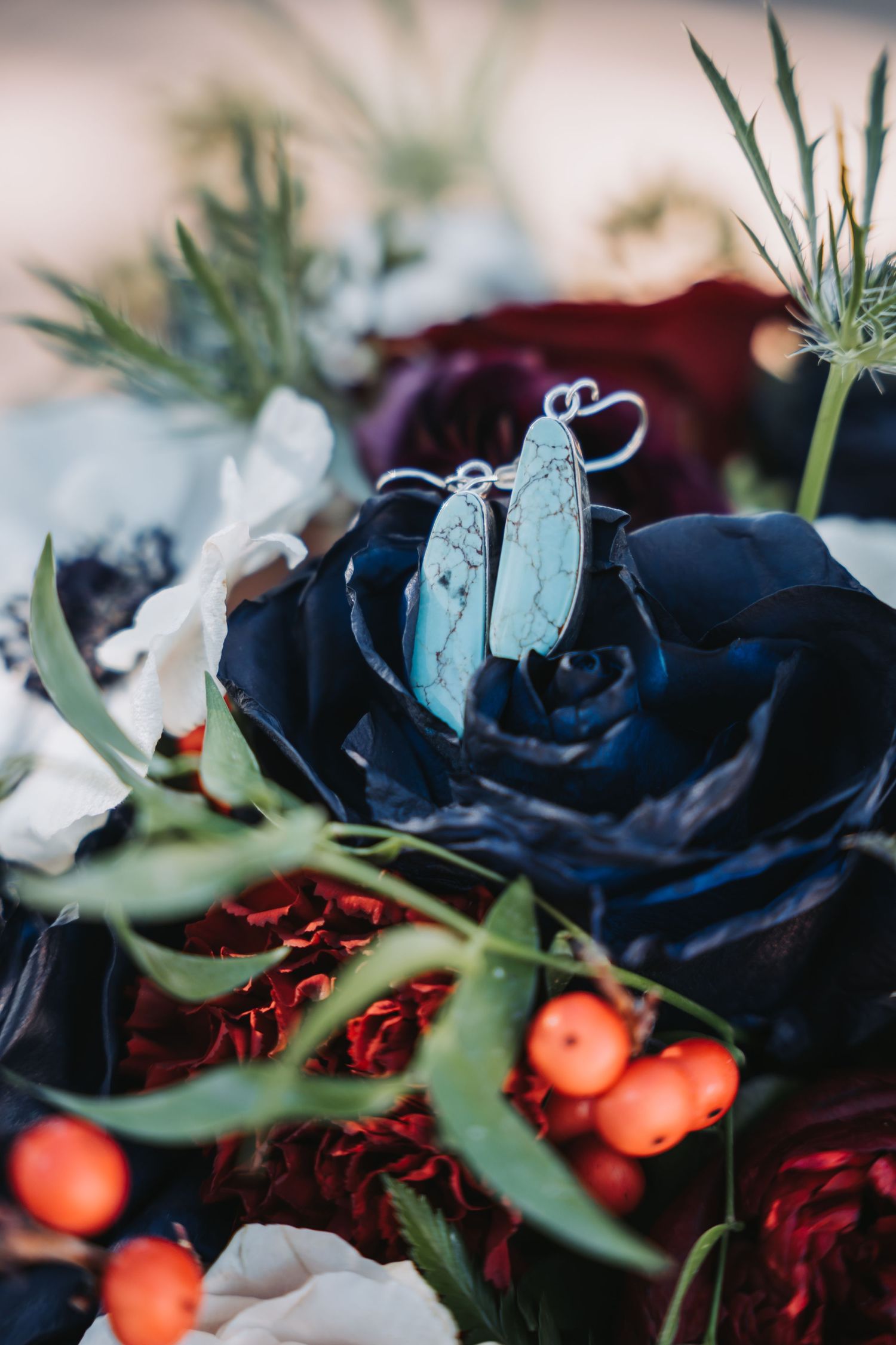 Blue silk rose and orange berries in a dramatic wedding bouquet with turquoise earrings.