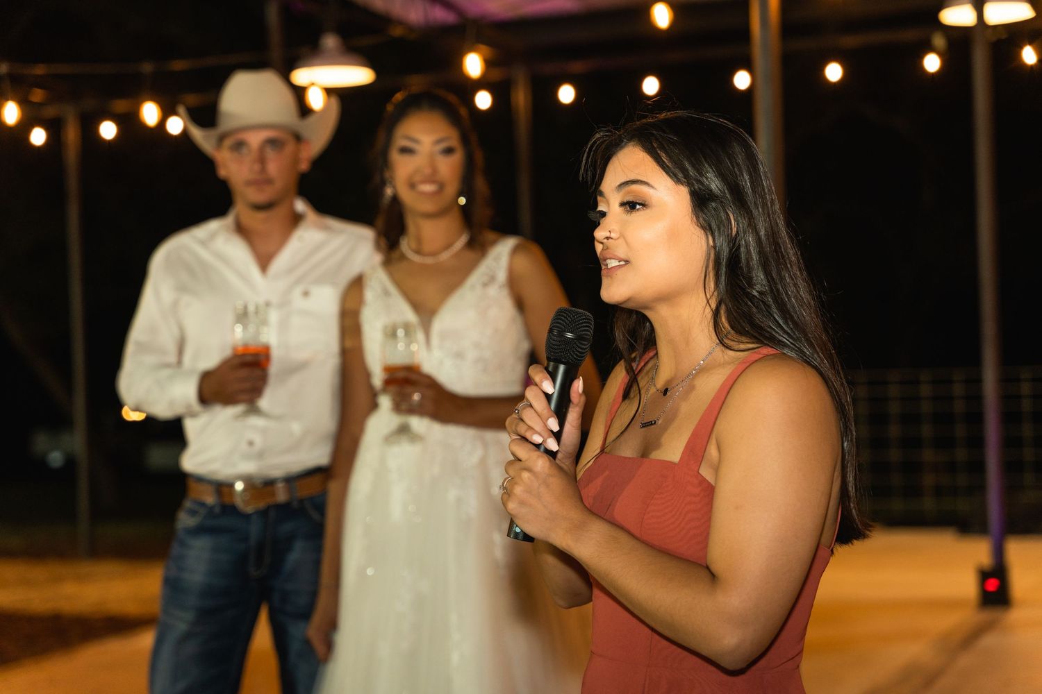 A wedding reception speech being given outdoors at night under string lights.