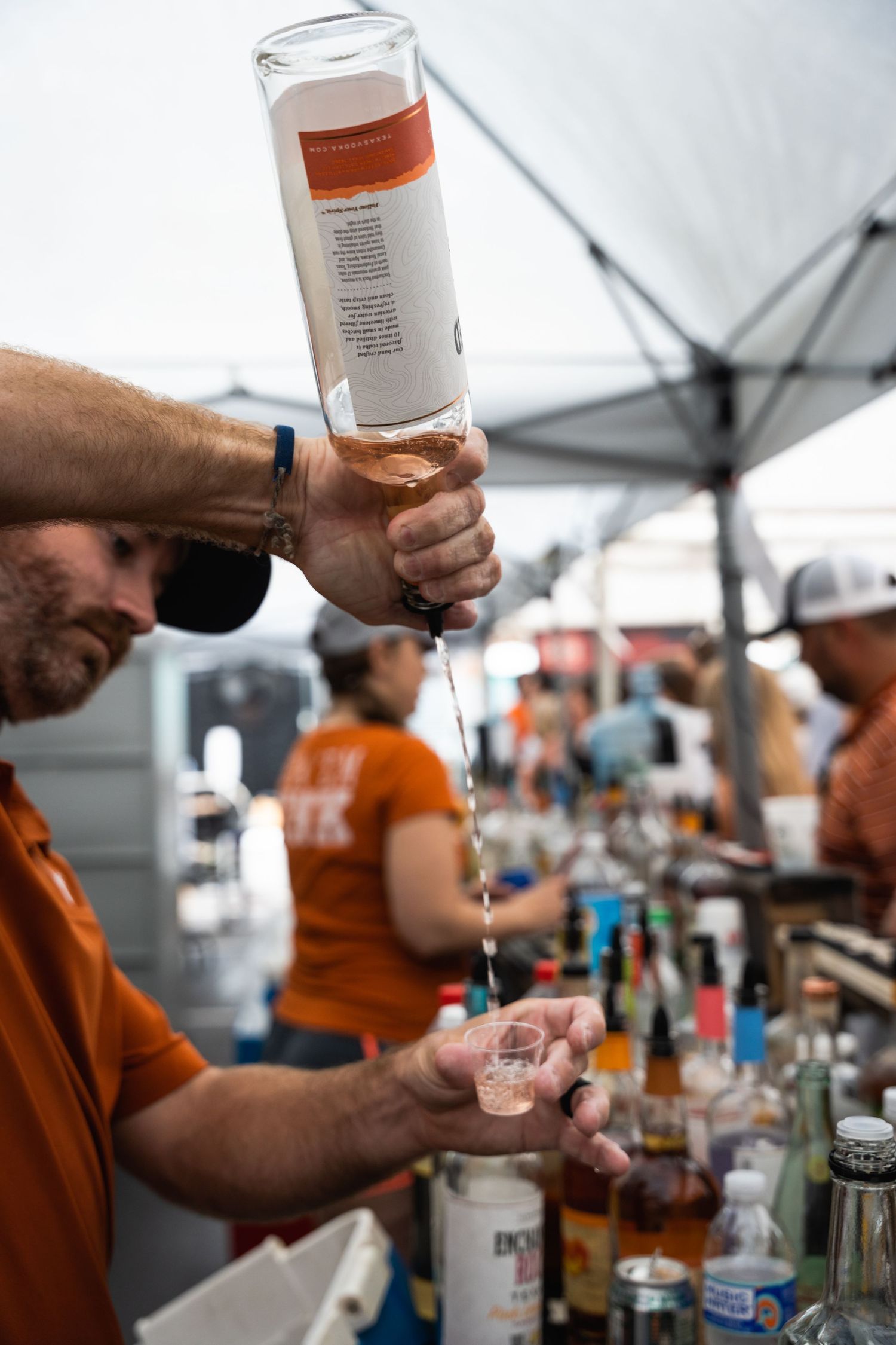 Close-up of hands pouring clear liquor from bottle at outdoor bar station.