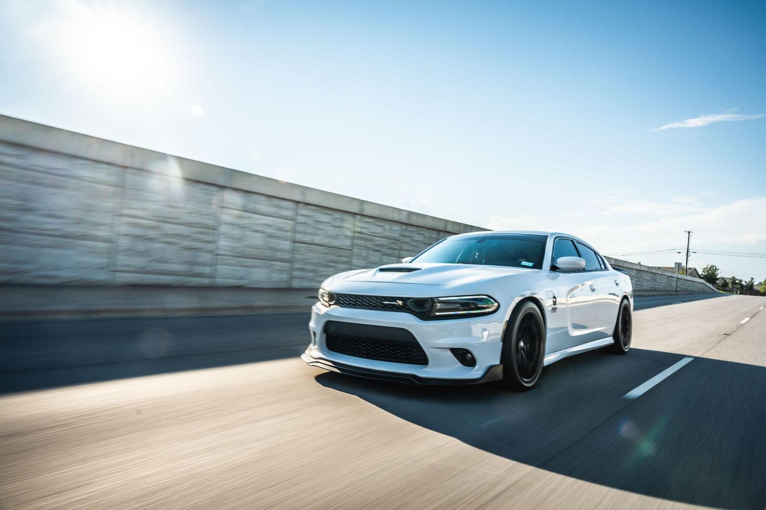 White Dodge Charger speeding past concrete barrier under bright blue sky.