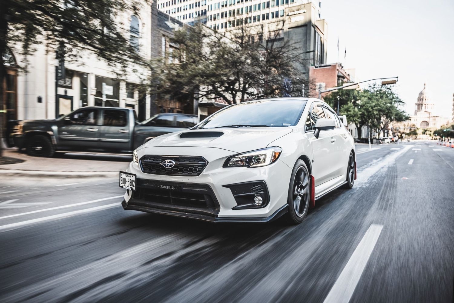 Pearl white Subaru WRX STI driving through city streets with motion blur effect.