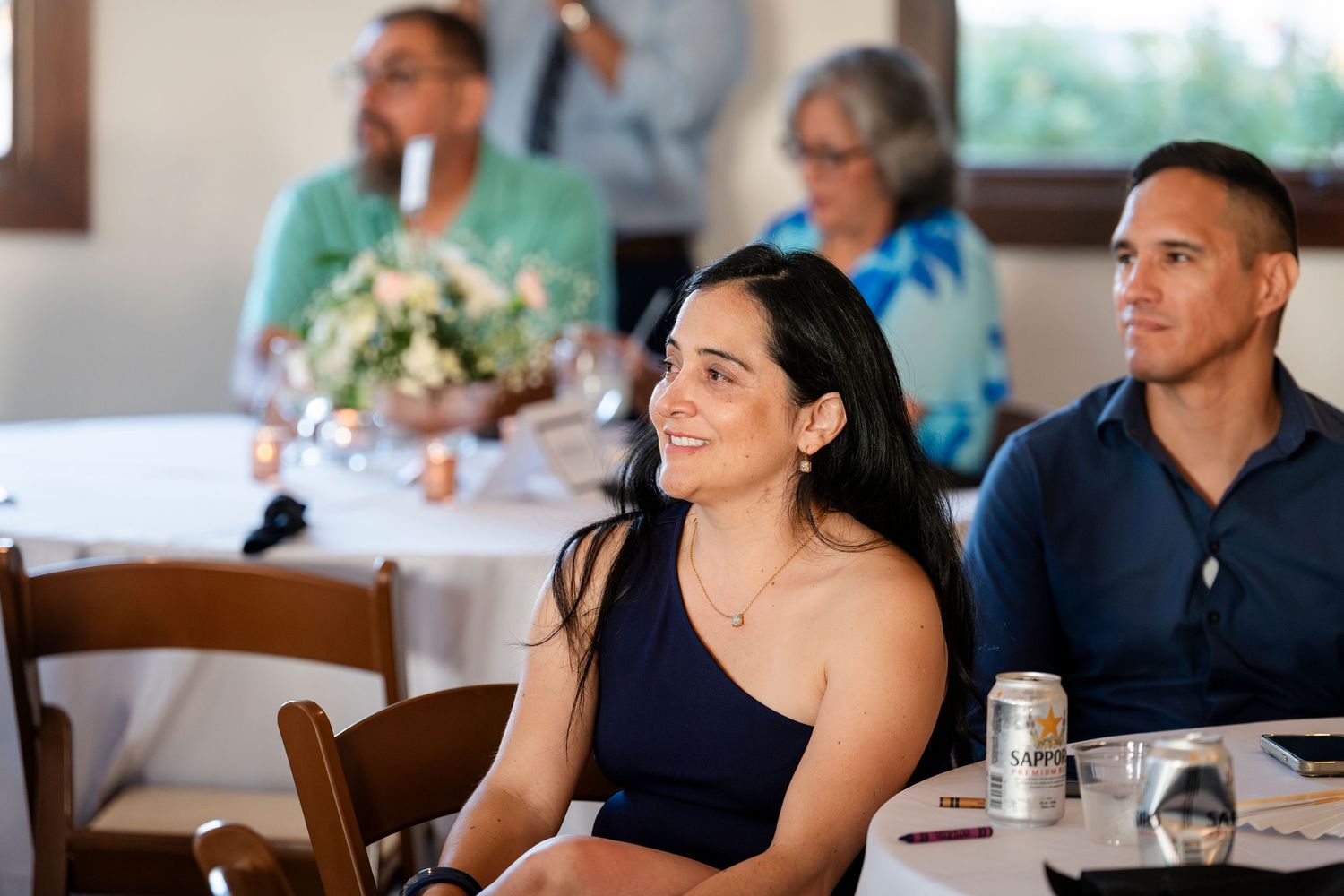 Wedding guests in casual attire sit at tables during a reception celebration.