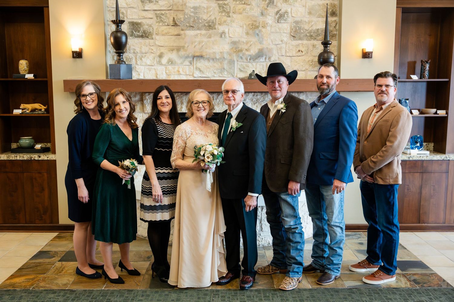 A group of wedding guests pose together in front of a stone wall inside an elegant rustic venue.