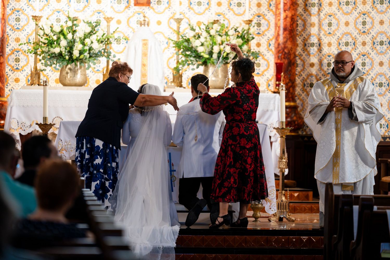 A wedding ceremony takes place at the altar with multiple participants gathered in a church setting.