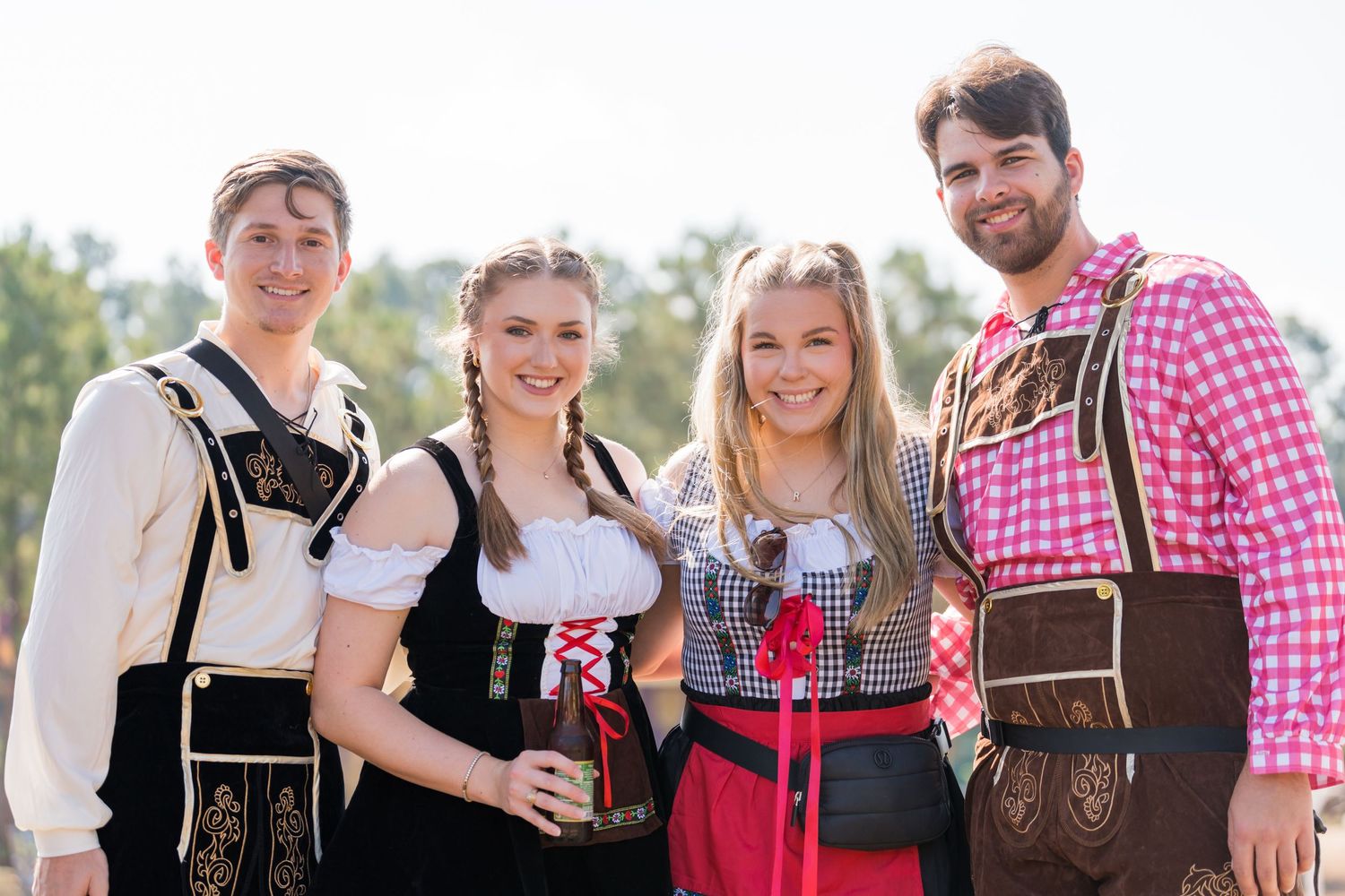 Group wearing traditional Bavarian outfits and lederhosen posing together outdoors.