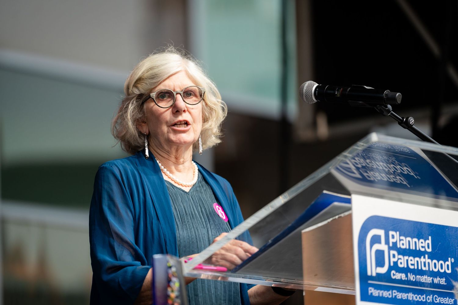 Speaker in blue delivers remarks at Planned Parenthood podium during outdoor event.
