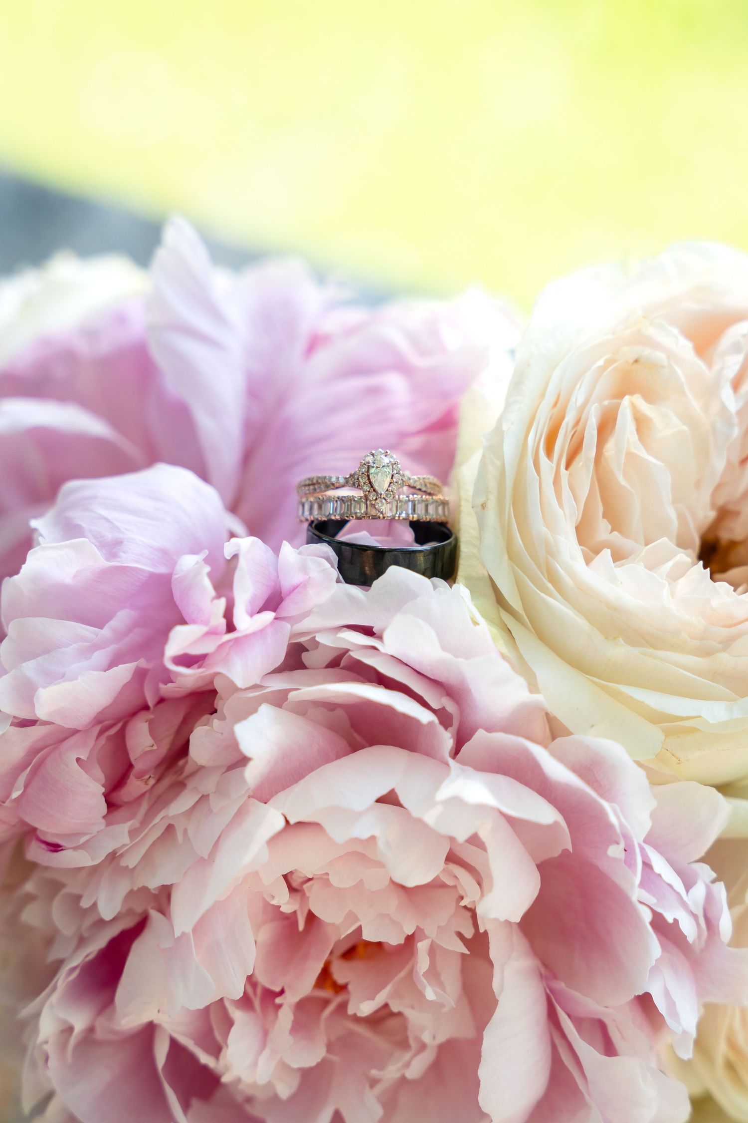 Diamond wedding rings nestled among soft pink and white peonies with natural lighting.