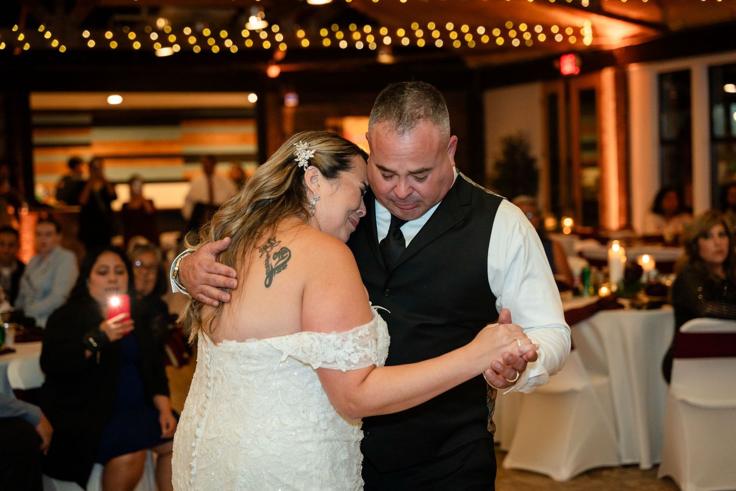 A couple shares an intimate slow dance at their wedding reception with string lights in the background.