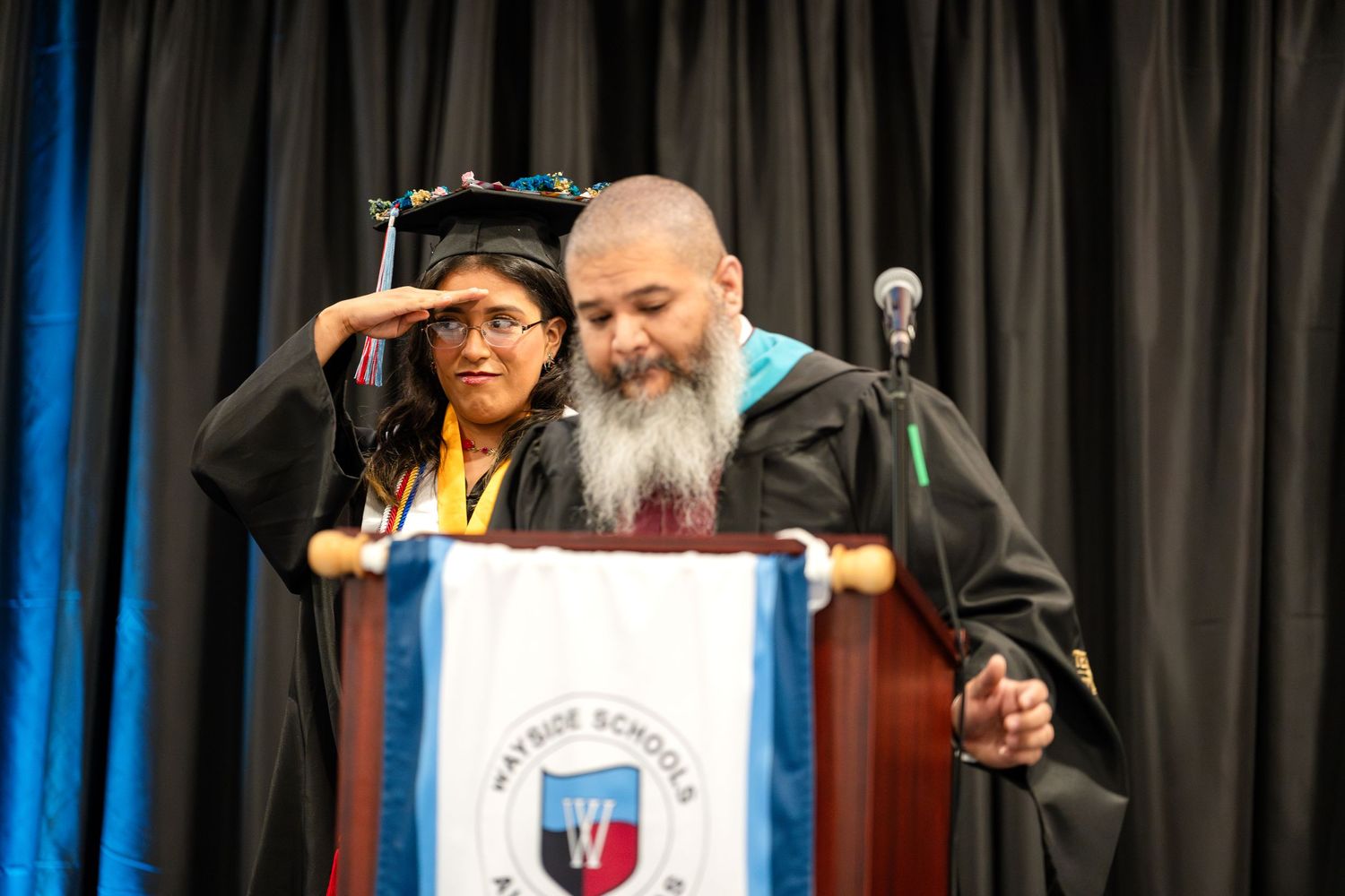 Two individuals sharing a moment at graduation podium during ceremony.