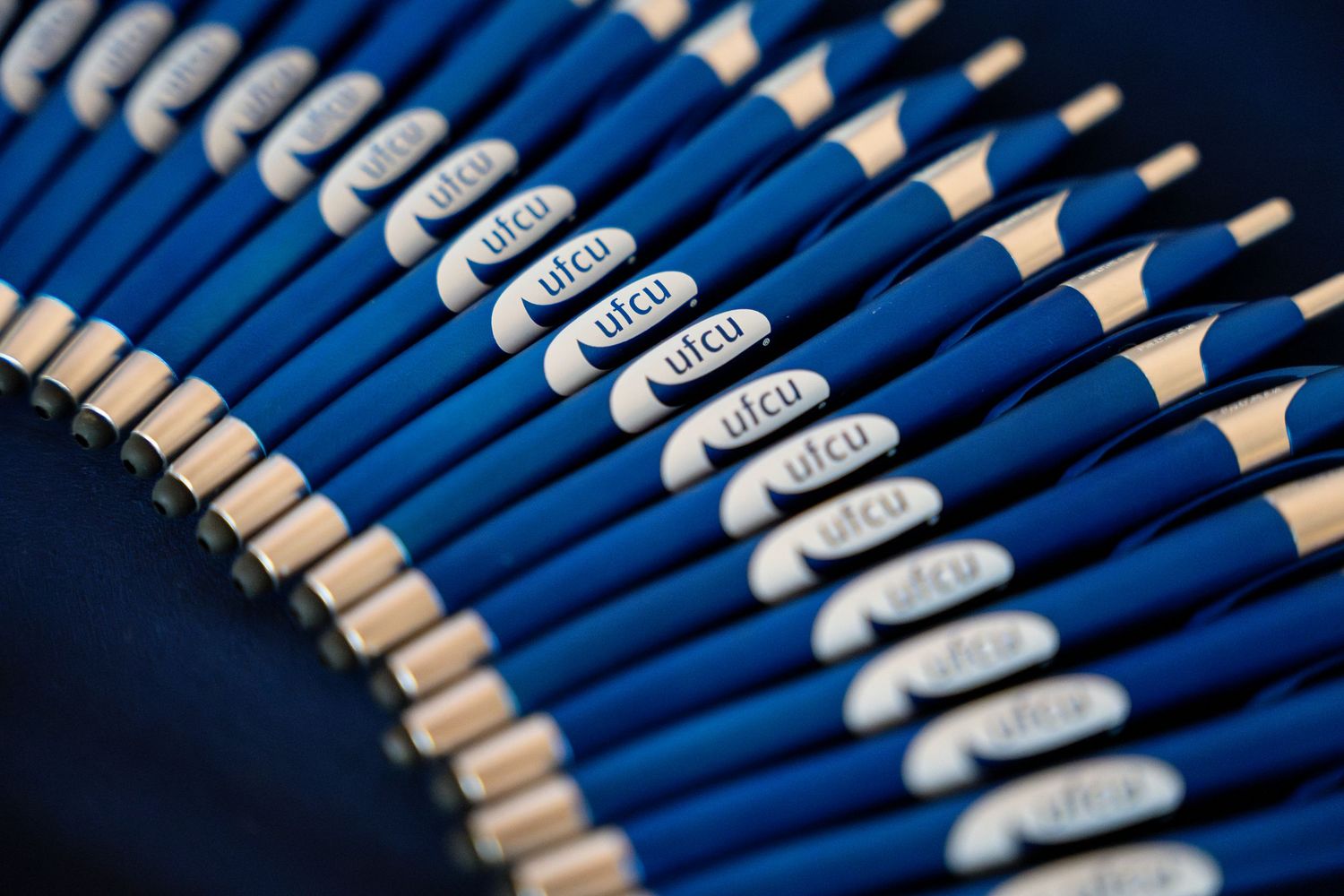 A row of identical blue pencils with white text arranged in a curved pattern against a dark background.