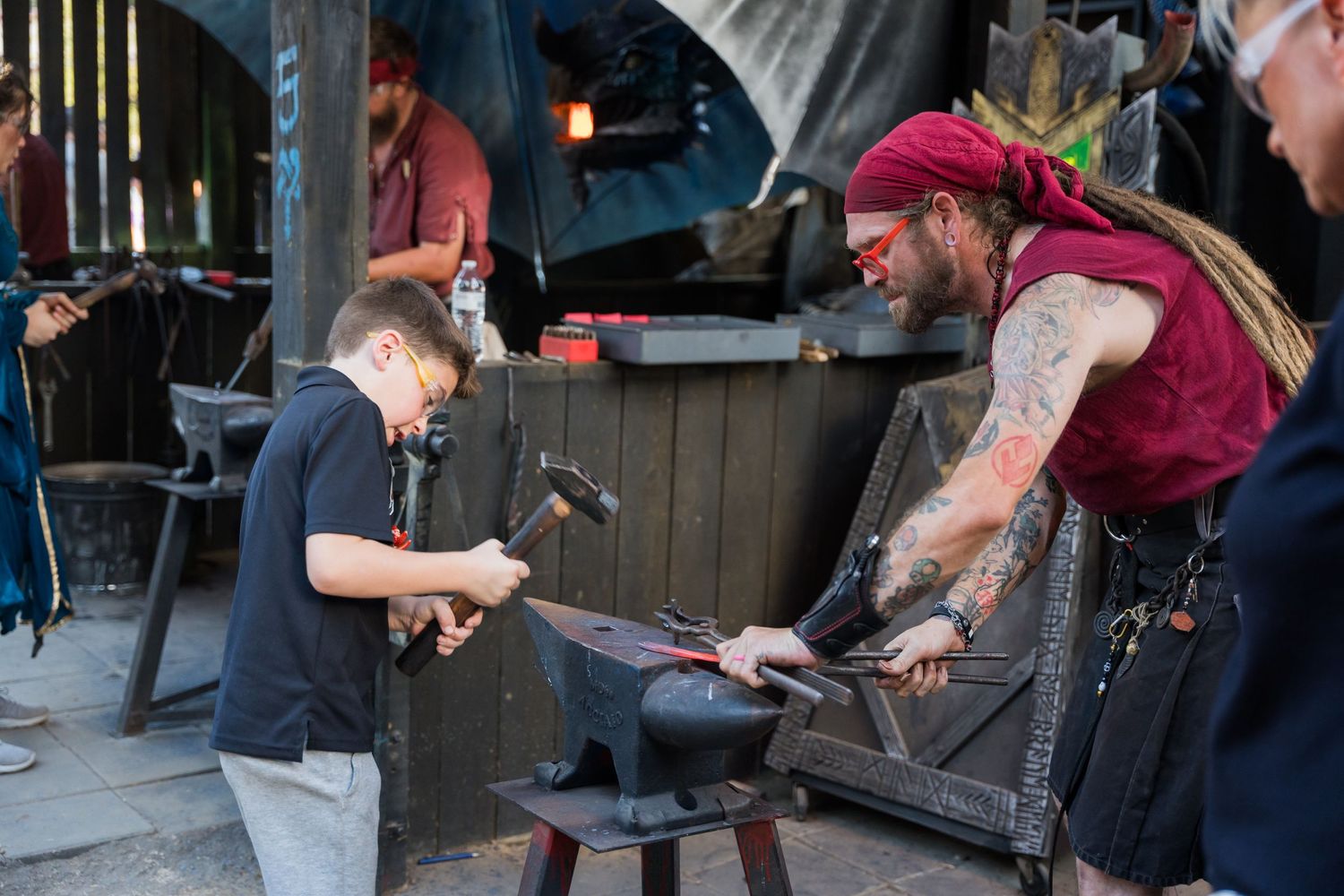 Craftsmen demonstrating traditional blacksmithing techniques at a medieval fair booth.