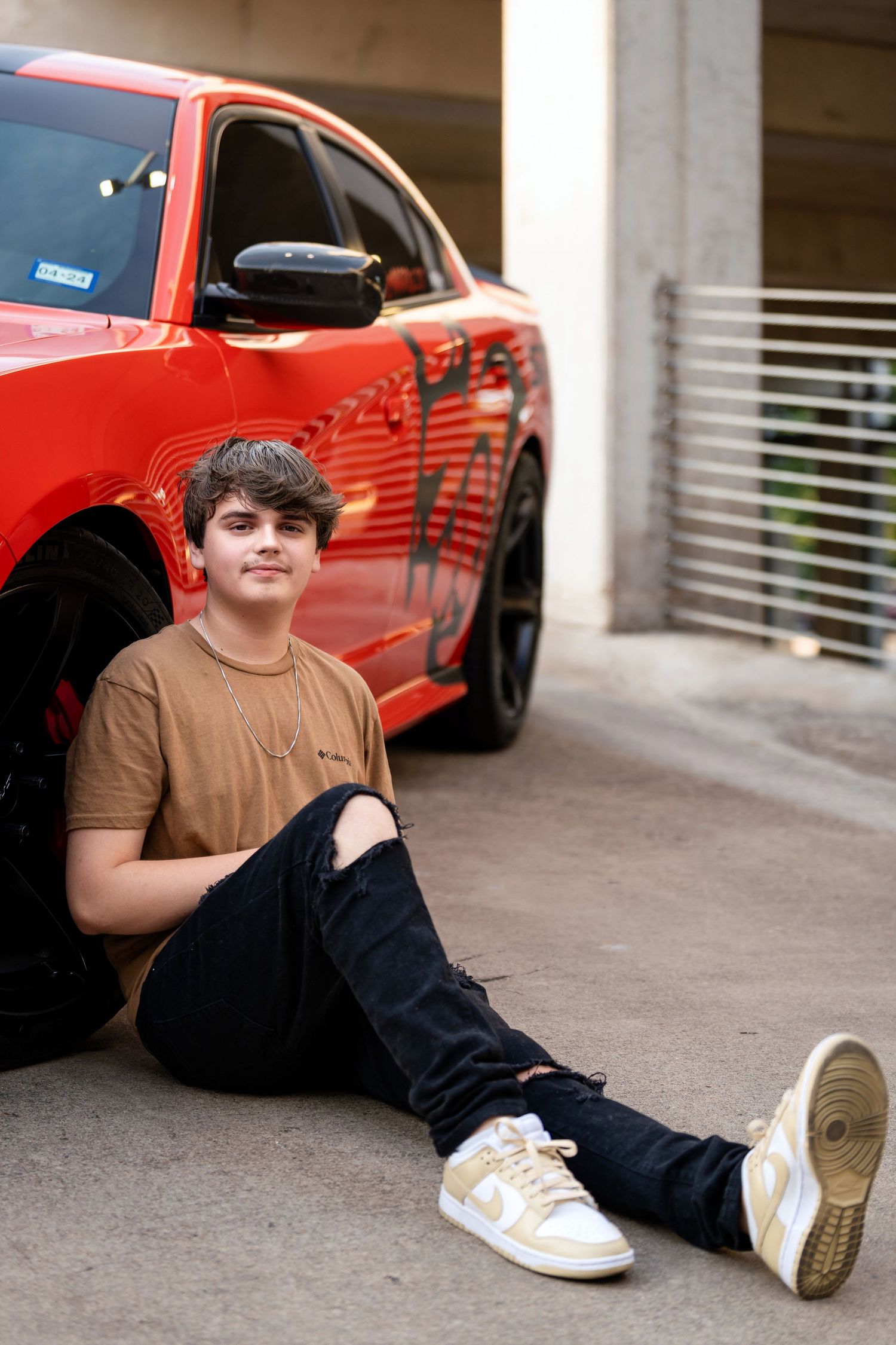 A portrait next to a bright red Dodge Charger with custom black graphics in a parking garage.