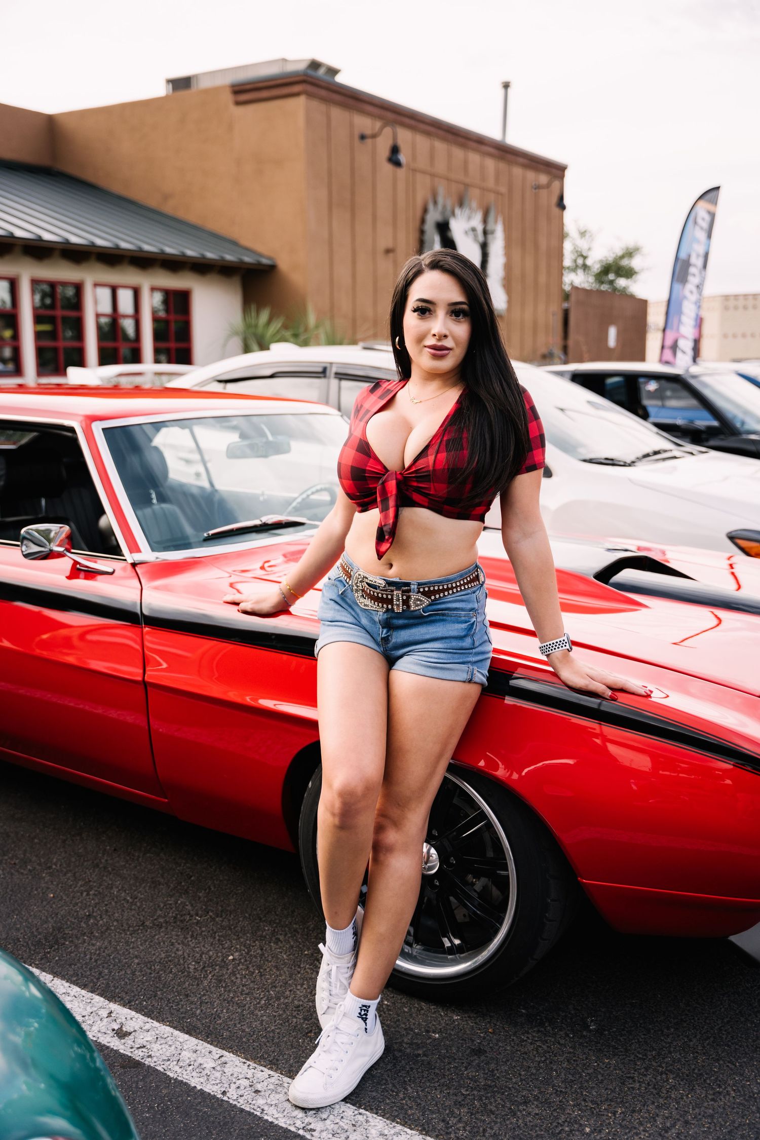 Car show featuring a classic red muscle car in a parking lot.