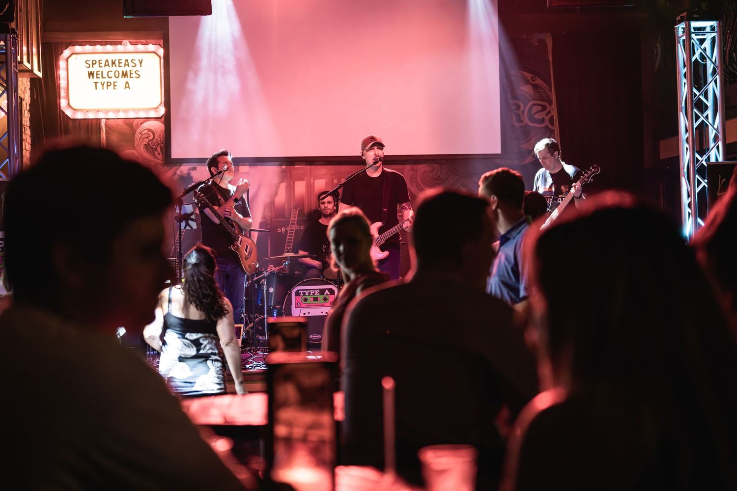 Band performing on stage with crowd silhouettes in foreground at an intimate venue.