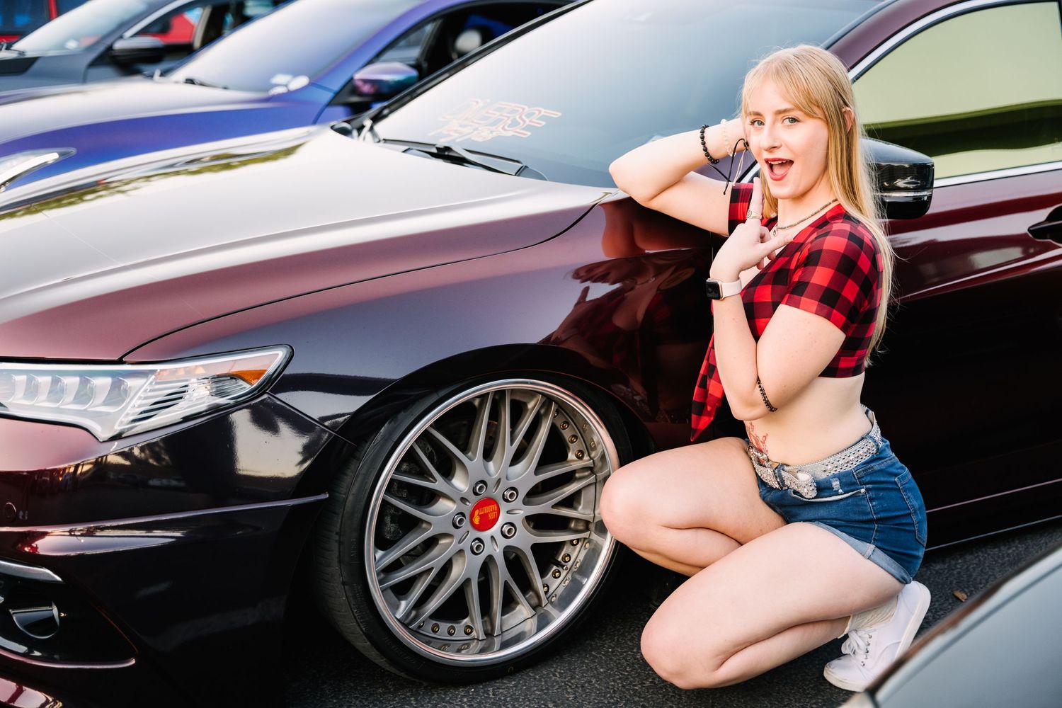 Car enthusiast poses next to black modified sports car with custom wheels.