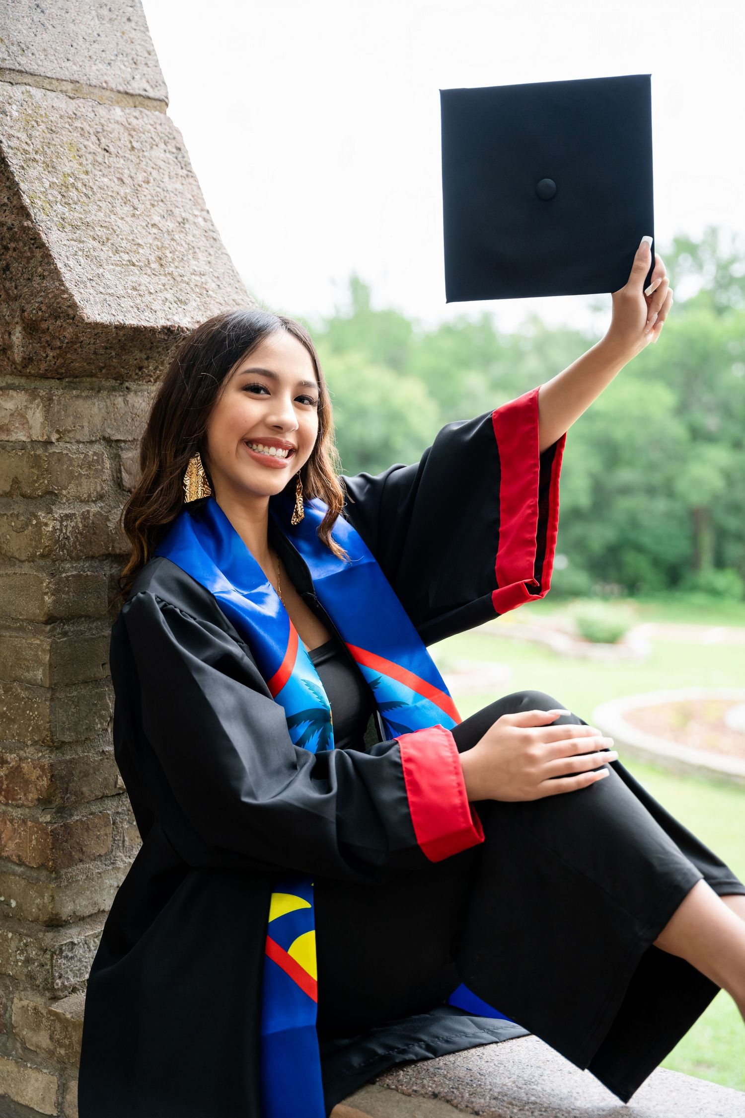 Graduate in traditional academic regalia poses with diploma on stone architecture.