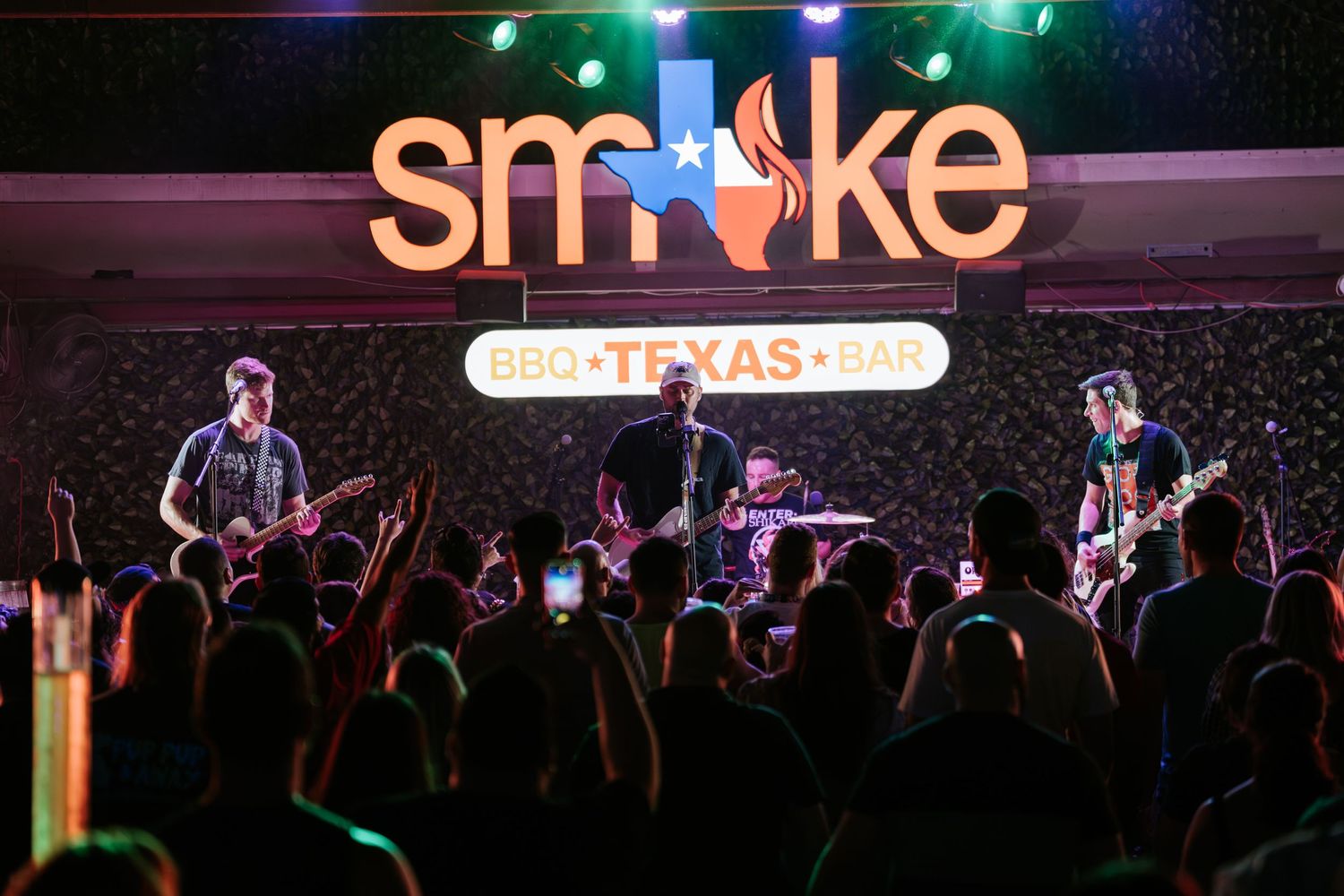 Live band performing under colorful lights with Smoke BBQ Texas signage above.
