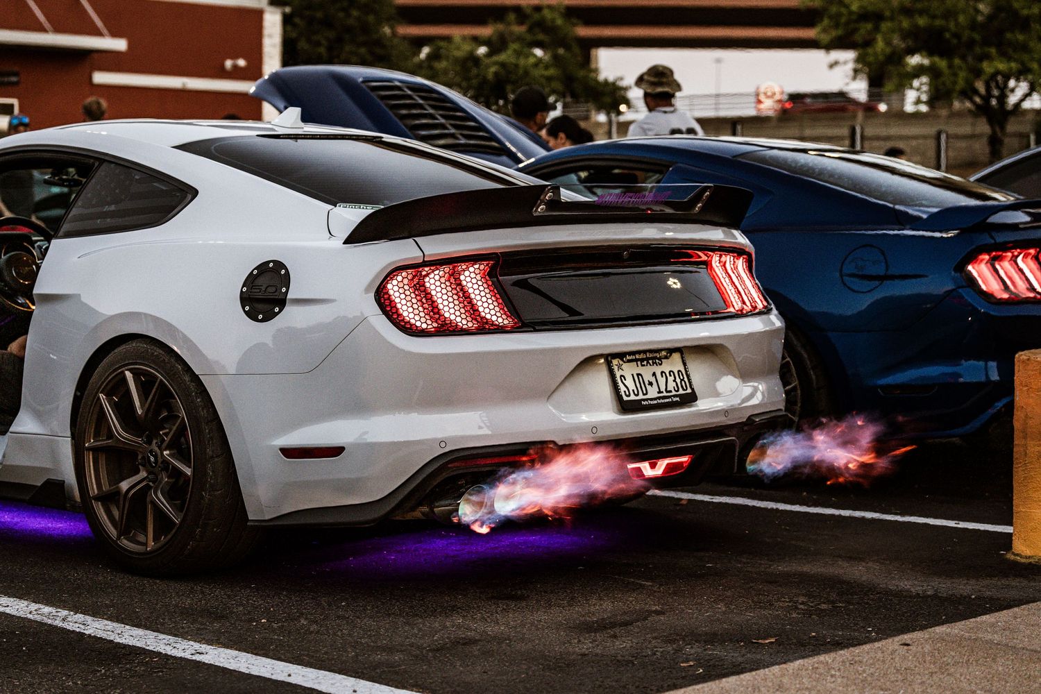 White Ford Mustang shooting flames from exhaust in parking lot at night.