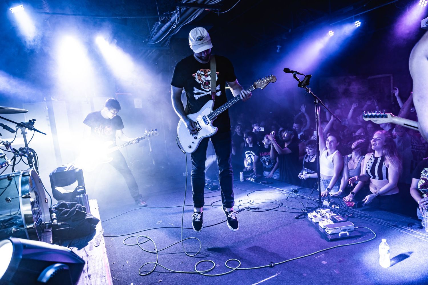 Guitarist performs on stage with bright blue spotlights and smoky atmosphere at a live music venue.