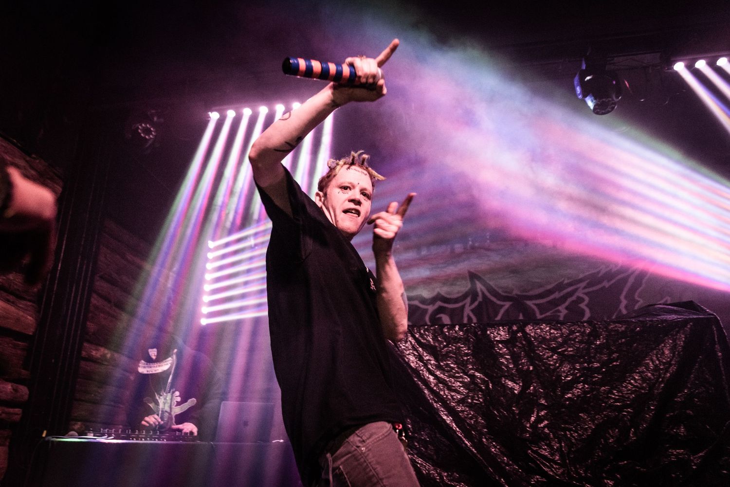 Concert performer raising microphone with purple lighting and smoke effects on stage.